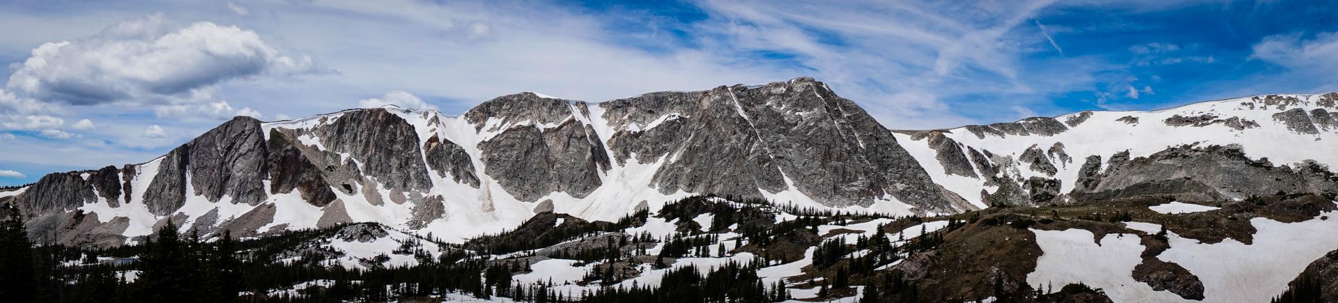 Panoramic view of rugged, snow-dusted mountains under a bright, cloudy sky.