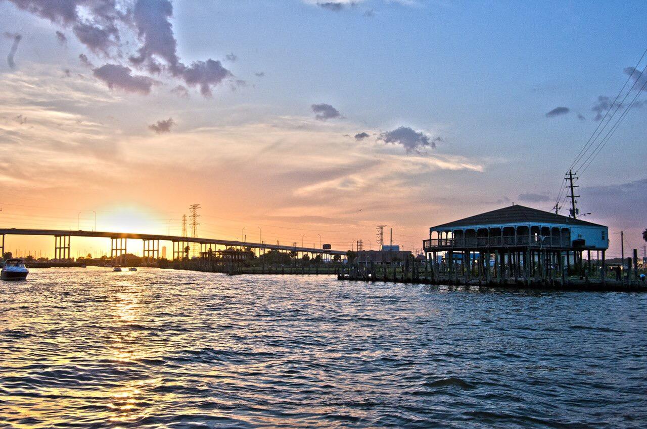 Sunset over water with a stilt house, bridge, and boats.