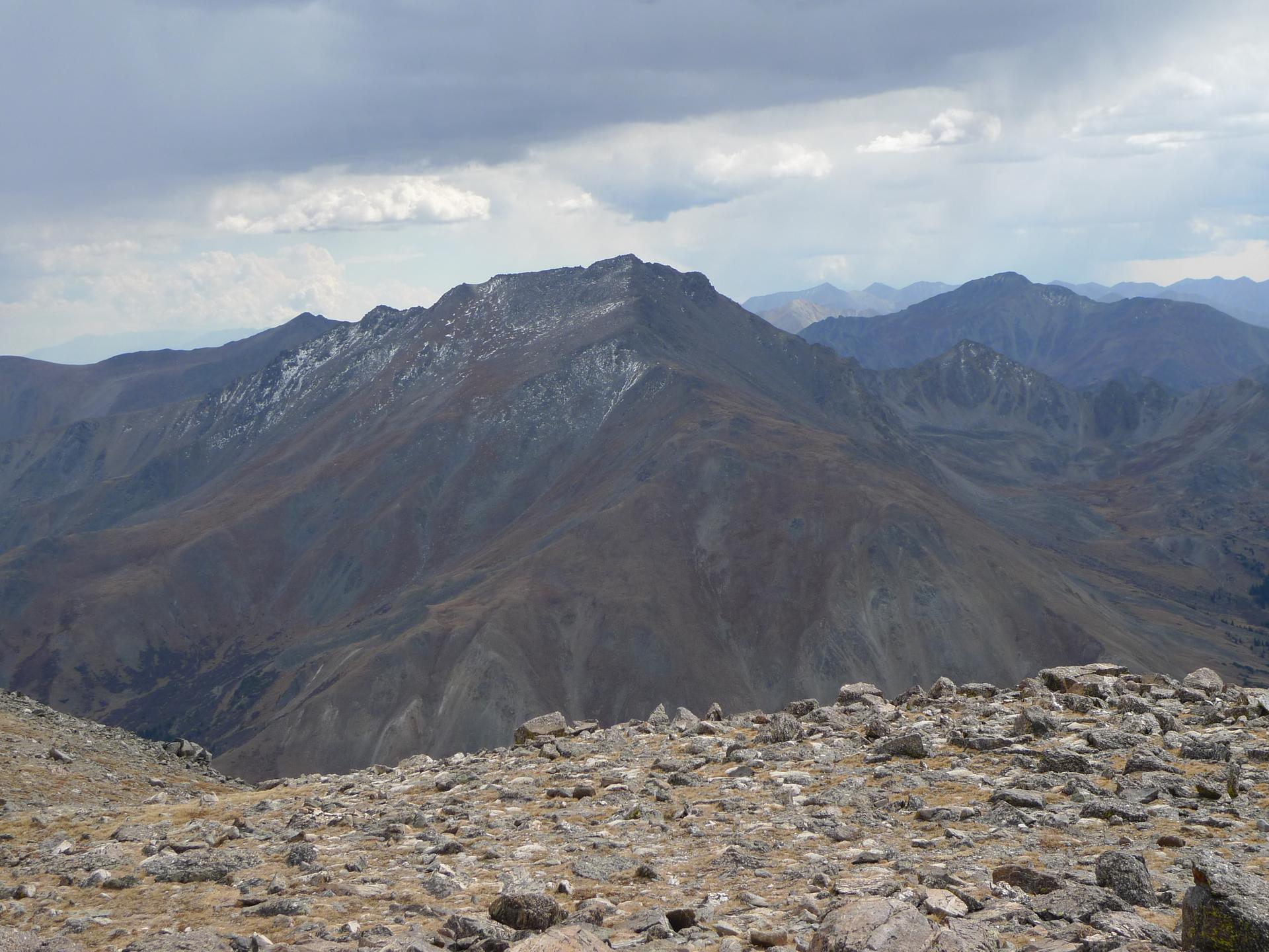 Vast, rugged mountain range with rocky foreground under an overcast sky.