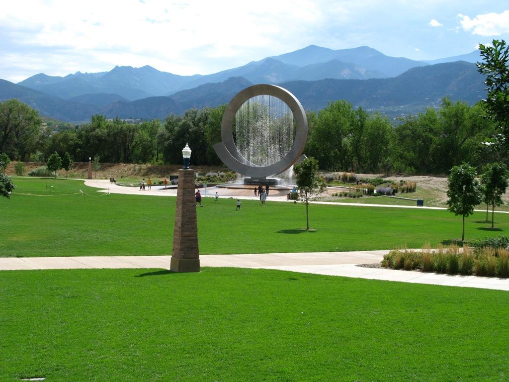 Modern circular sculpture in a green park with mountains in the background.