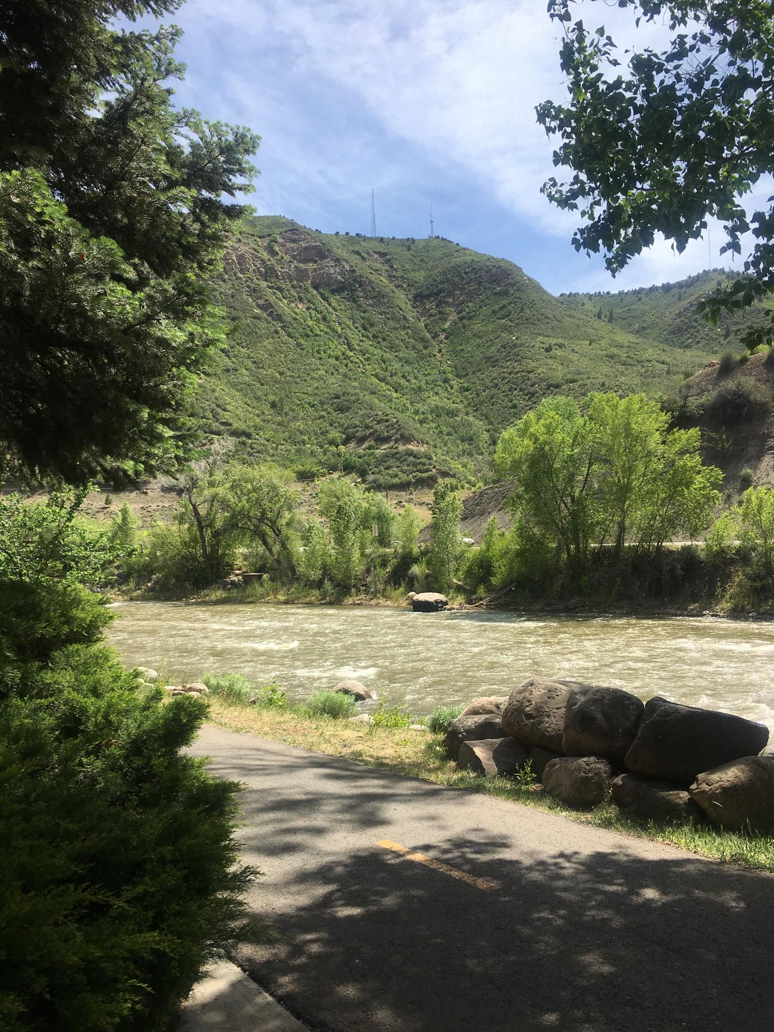A river flows past green mountains under a bright, partly cloudy sky. - Animas River Trail