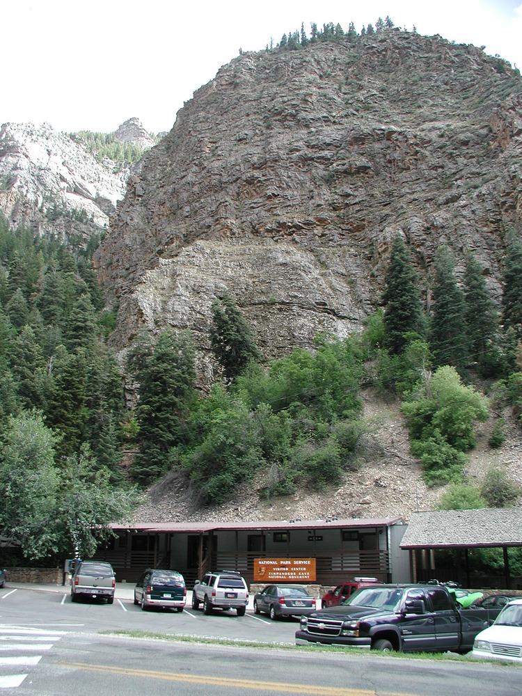 Cars parked in front of a building at the base of a massive rocky cliff.