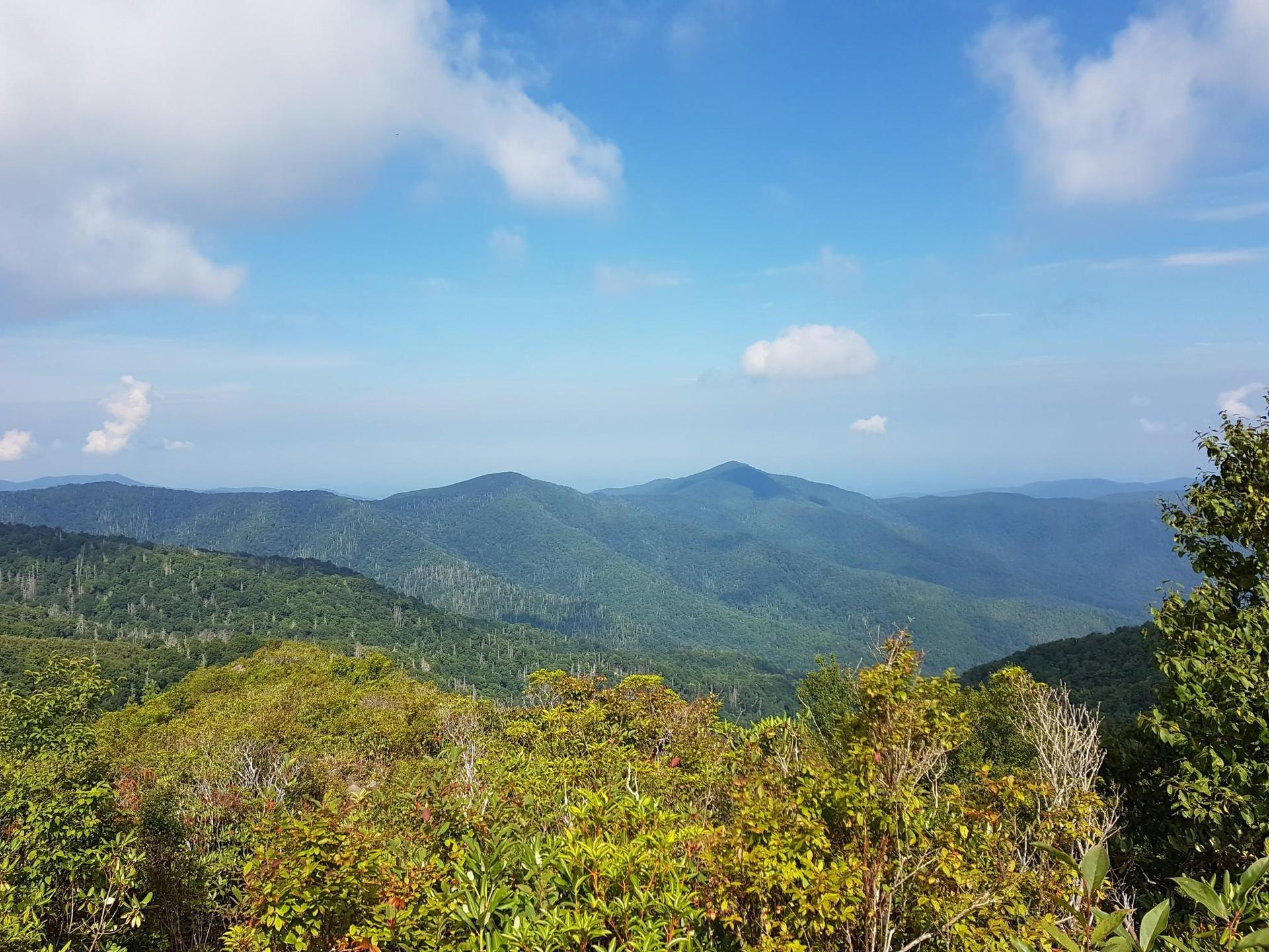 Expansive view of green mountains under a bright blue sky with scattered clouds.