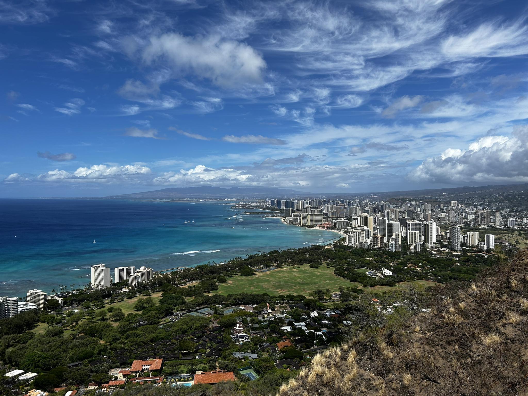 Panoramic view of a coastal city with skyscrapers, ocean, and blue sky.