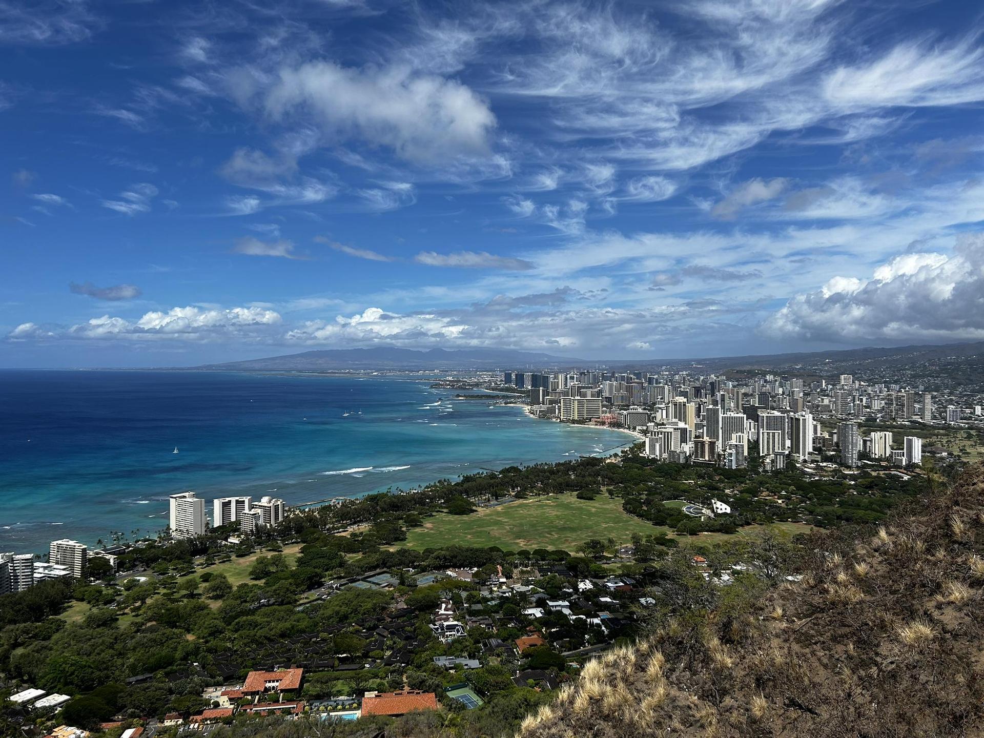Panoramic view of a coastal city with skyscrapers, ocean, and blue sky.