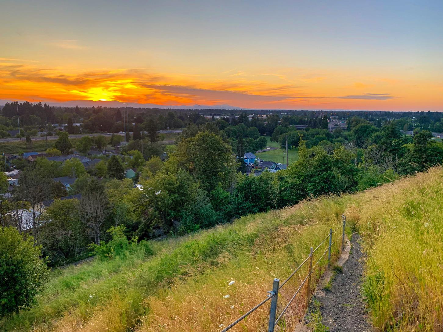 Golden sunset over a town, seen from a grassy hillside path.