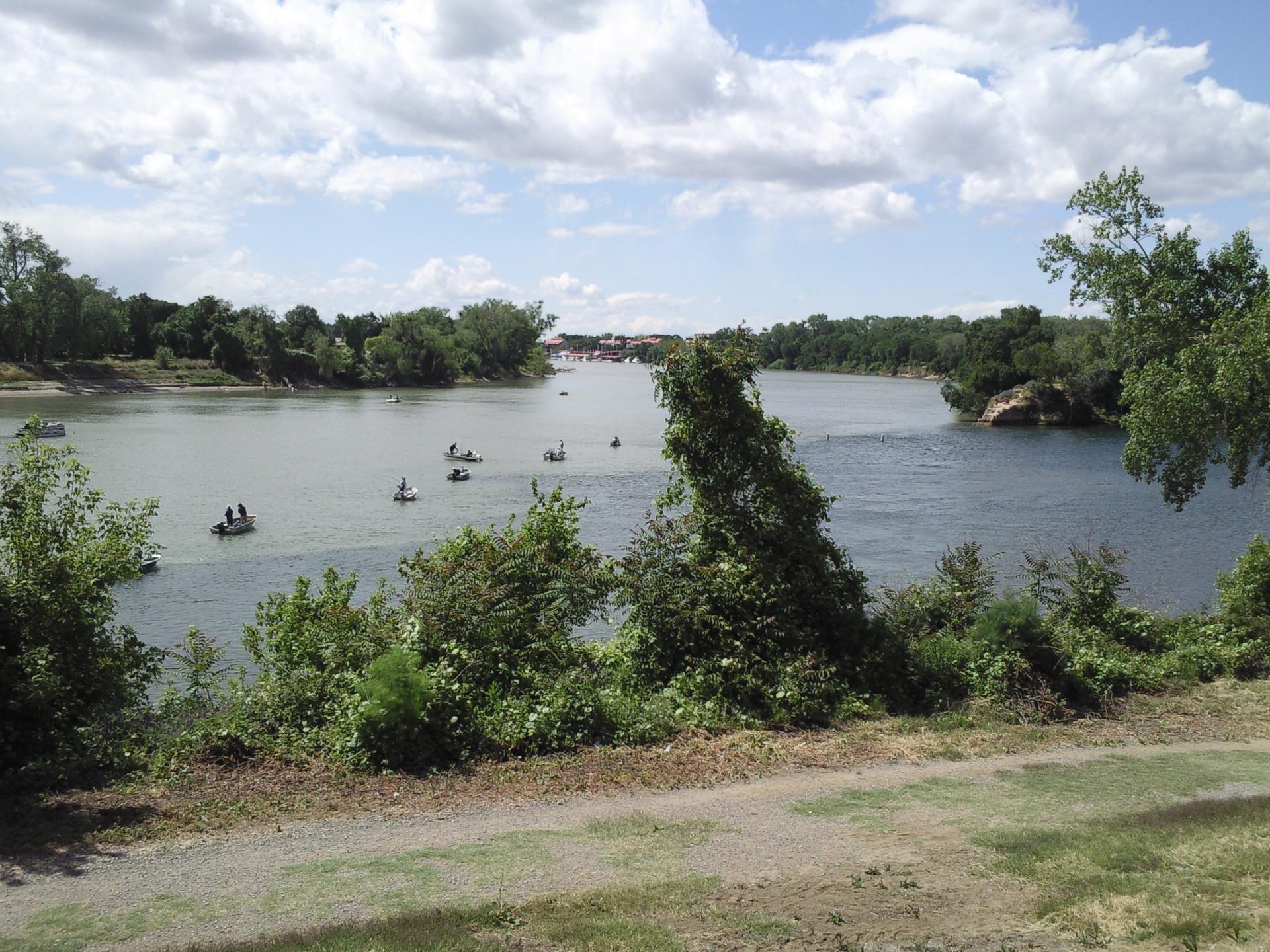 Boats on a wide river lined with green trees under a partly cloudy sky.