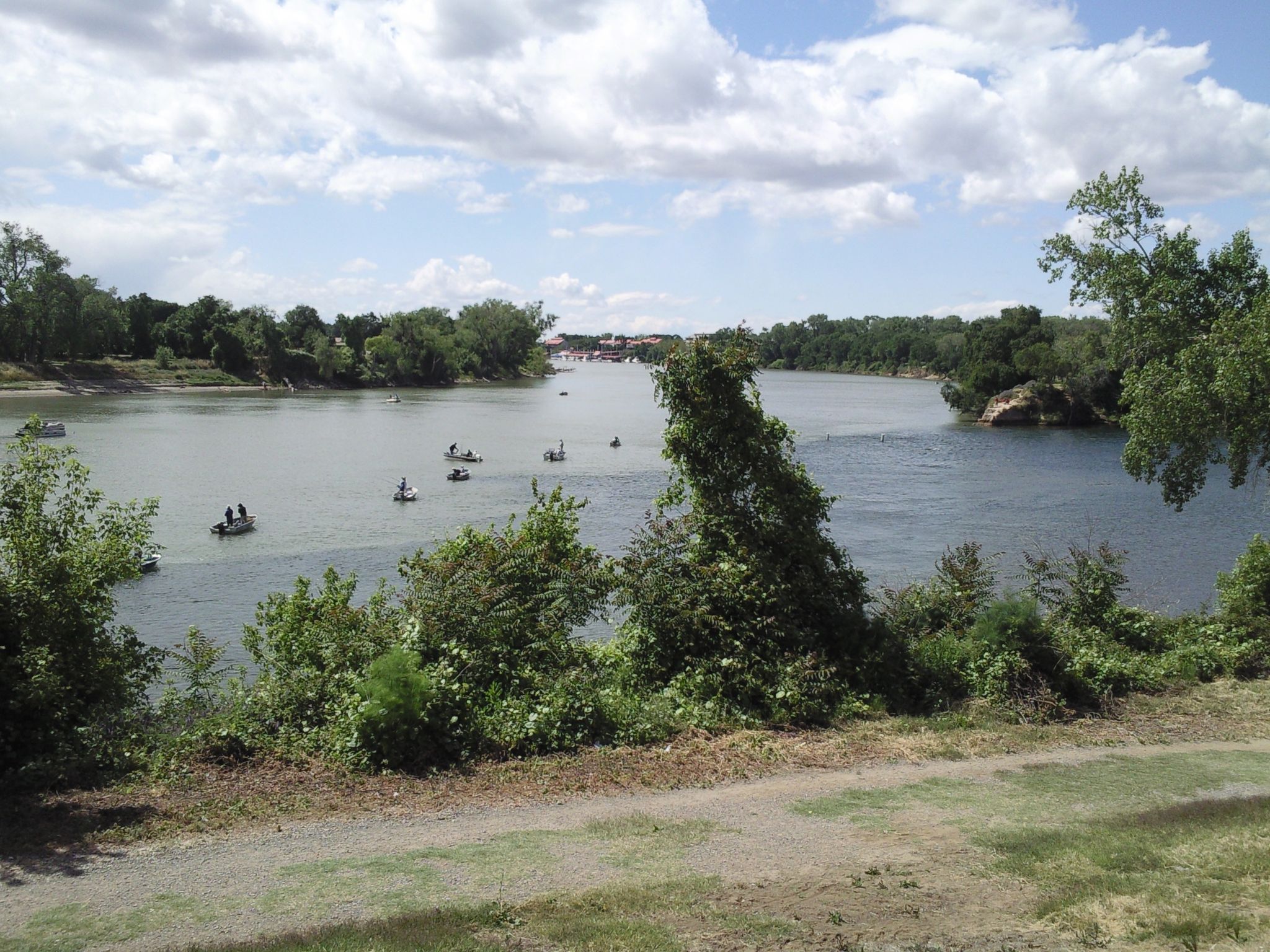 Boats on a wide river lined with green trees under a partly cloudy sky. - West Sacramento River Walk