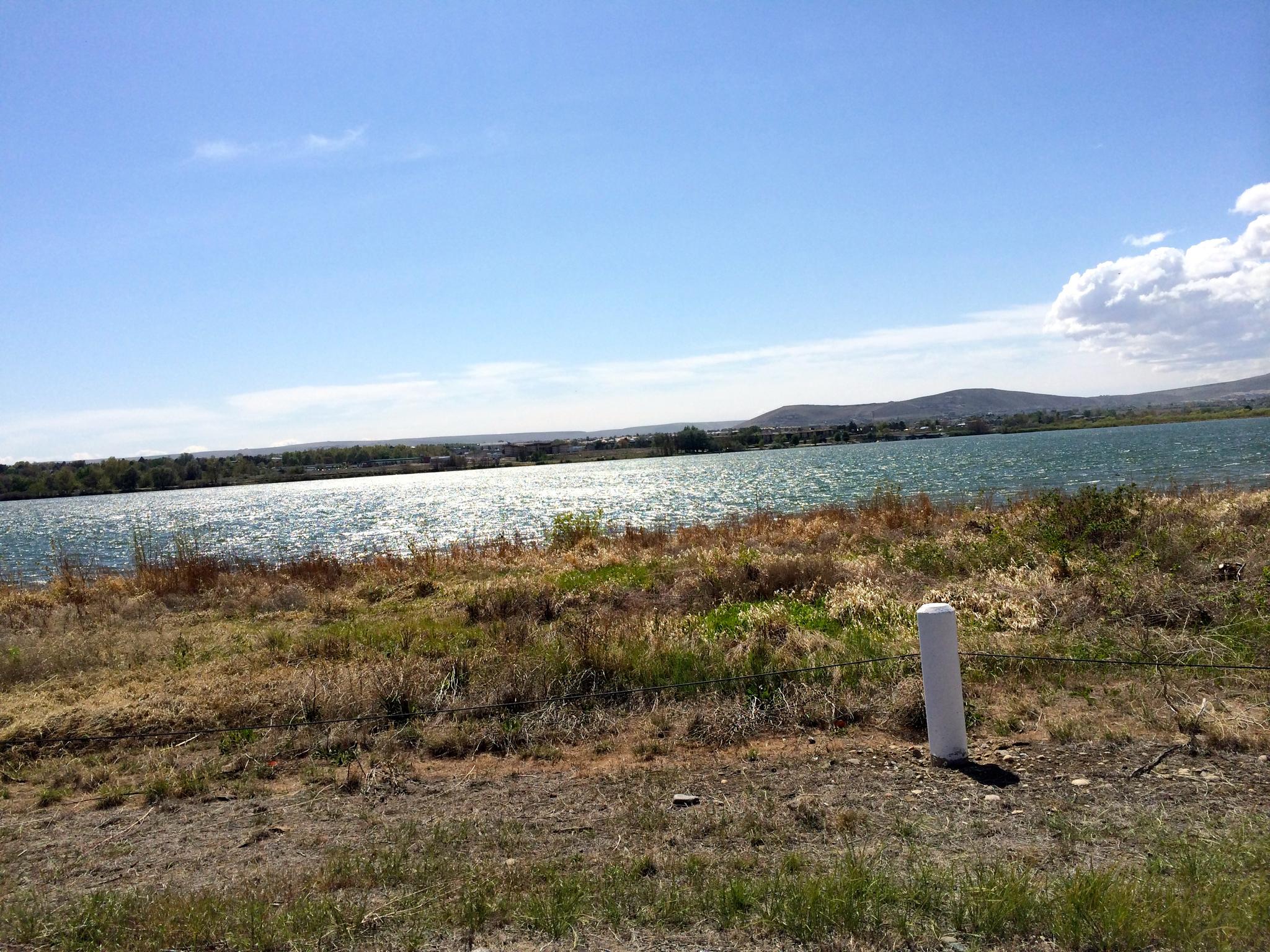 Sunlight glints on a wide body of water, with dry grass and distant hills.