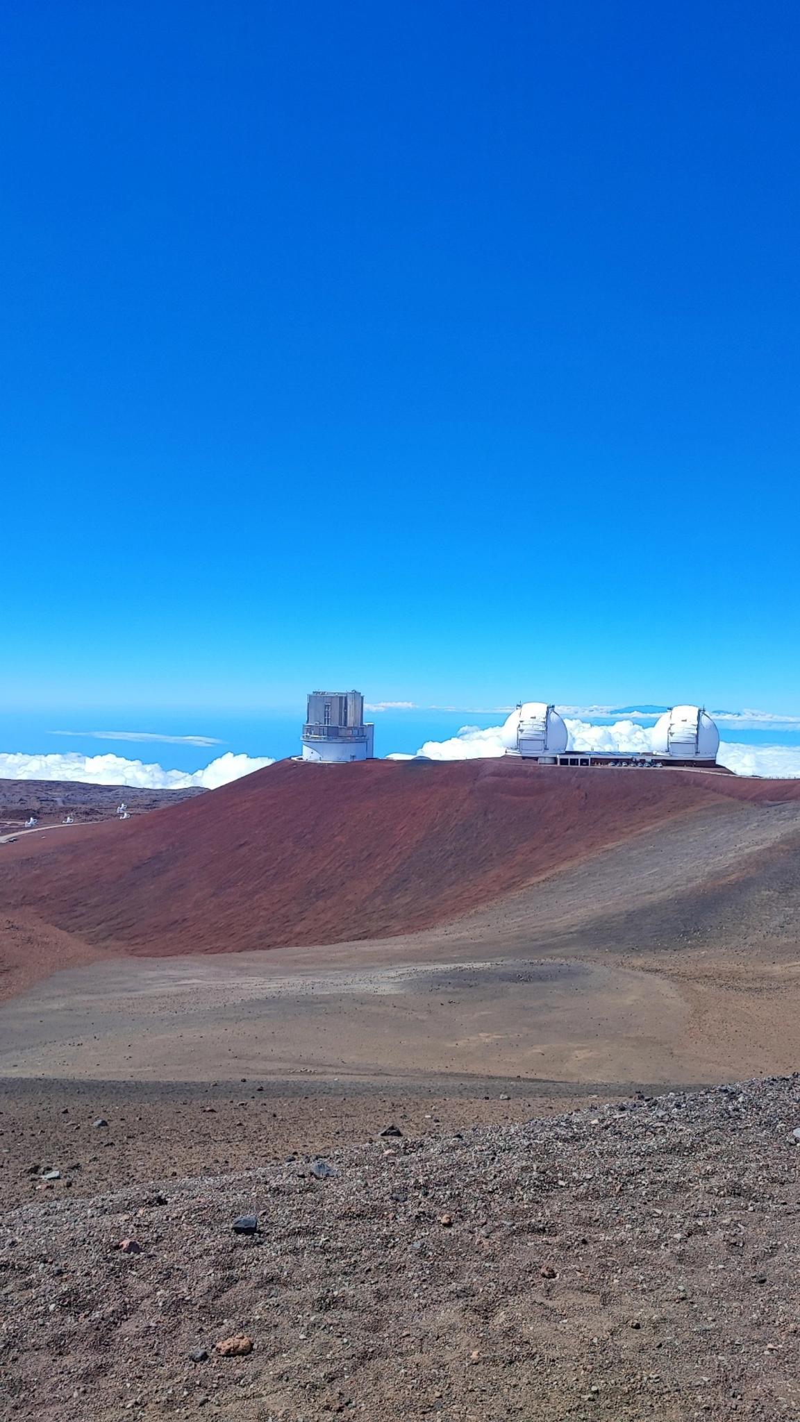 Two white observatories on a barren red mountain under a clear blue sky.