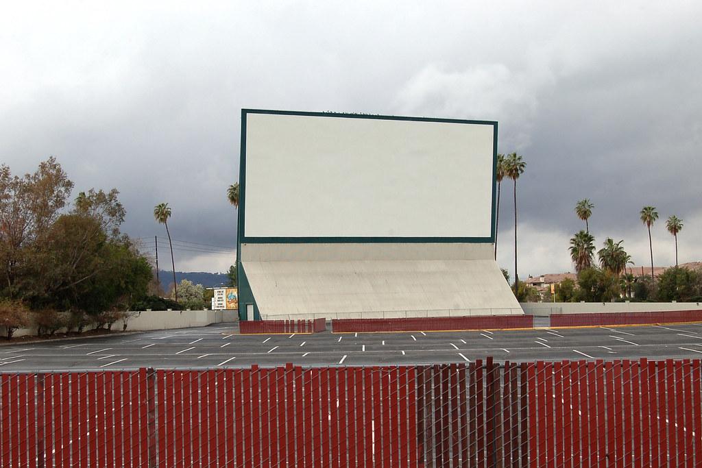Large empty drive-in movie screen under an overcast sky with palm trees.