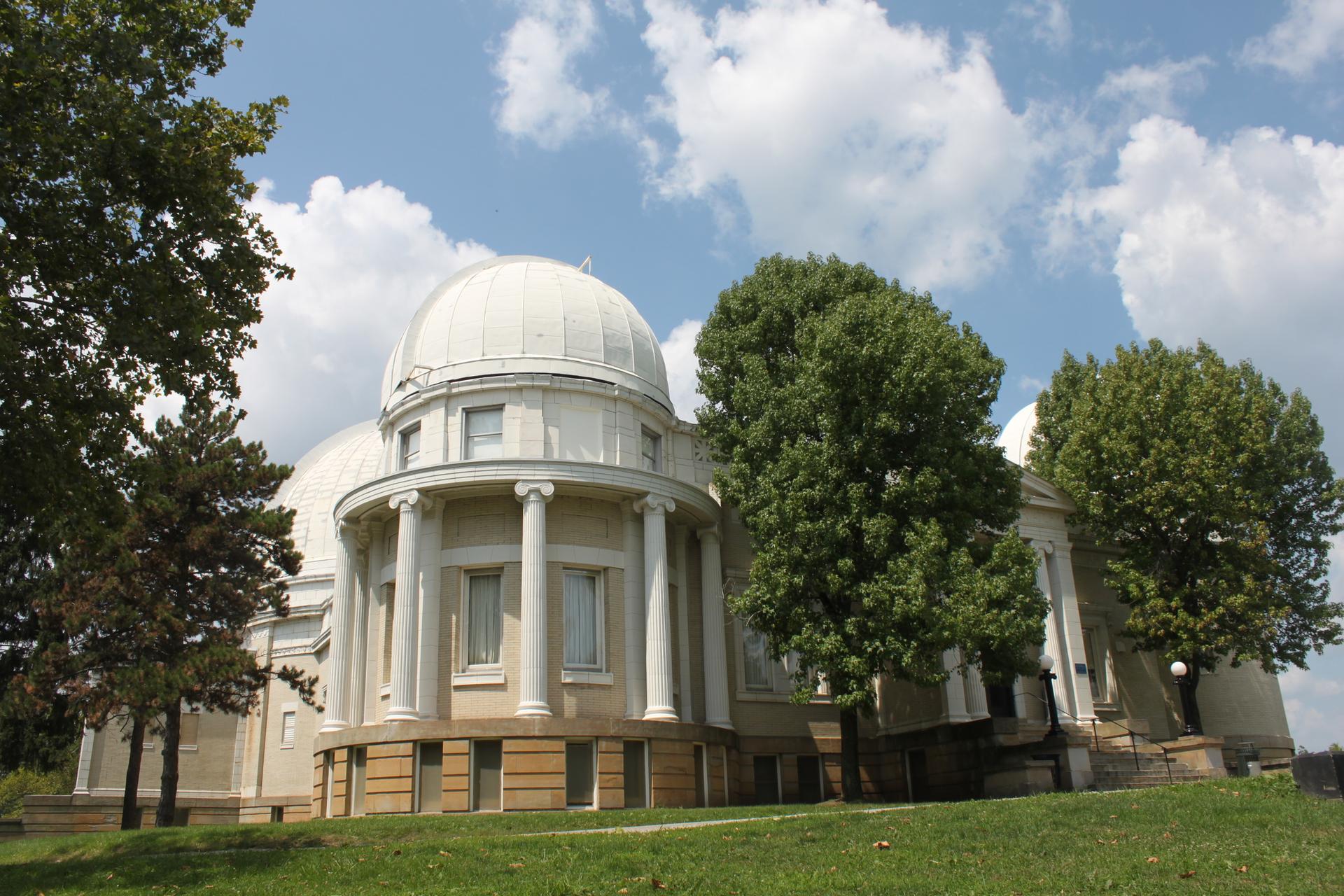 Large white domed building with columns on a grassy hill under a cloudy sky.