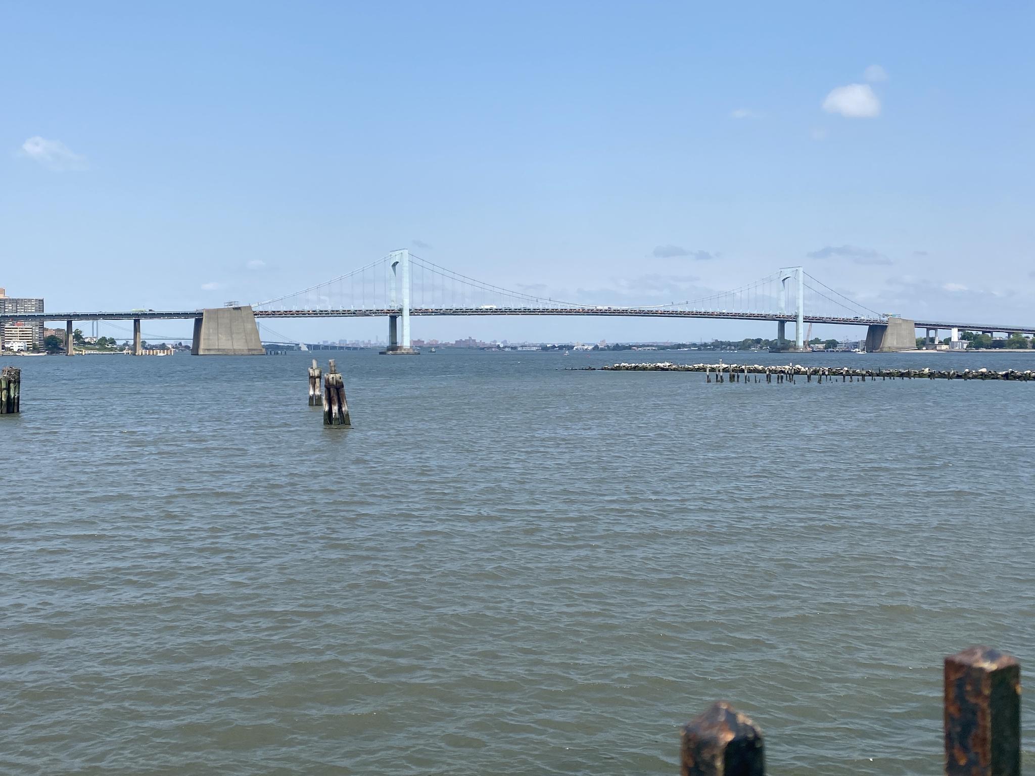 A large suspension bridge spans a wide body of water under a blue sky.