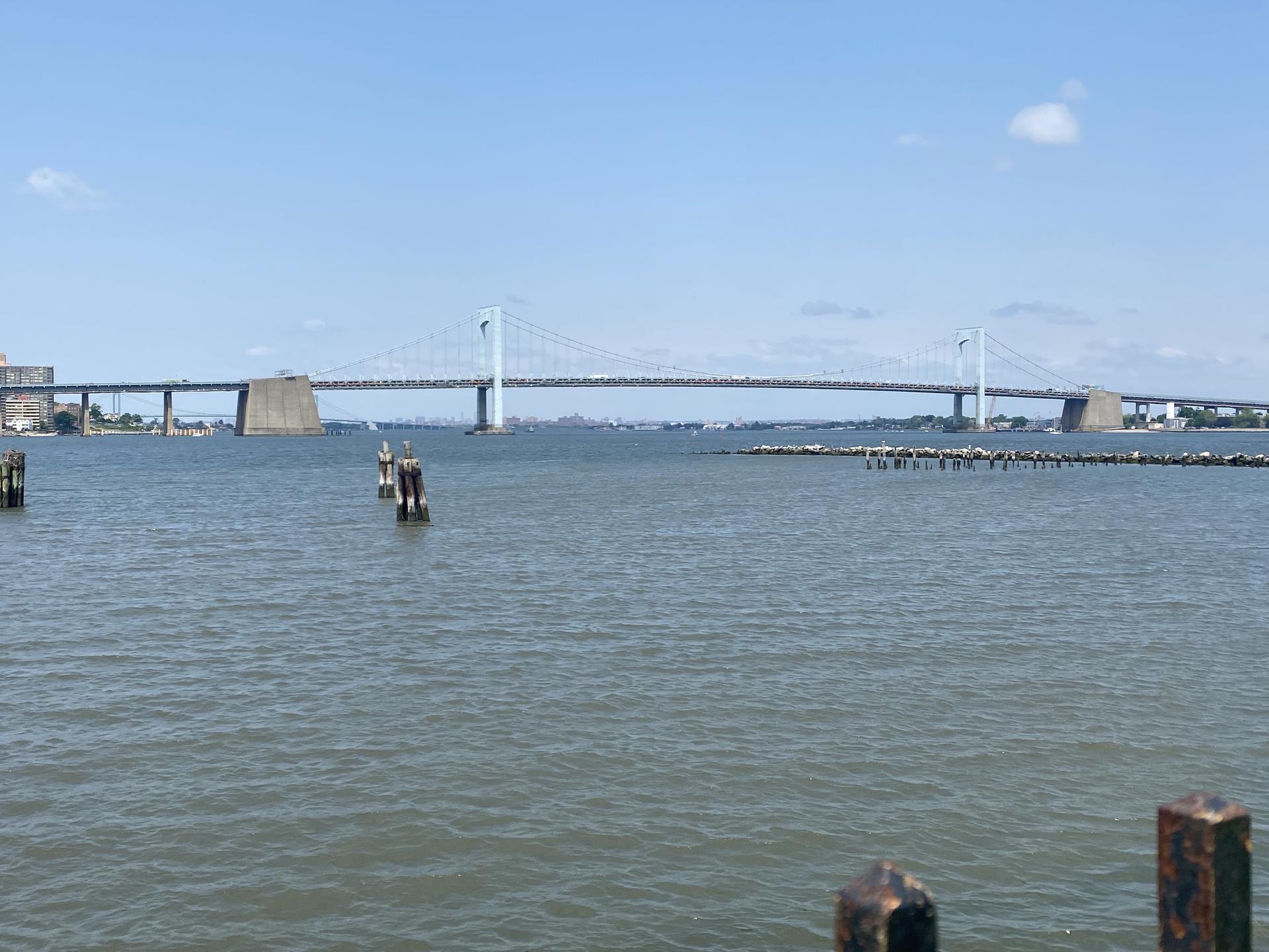 A large suspension bridge spans a wide body of water under a blue sky.