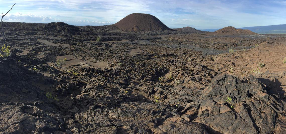 Vast, rugged lava landscape with a prominent cinder cone under a bright sky.