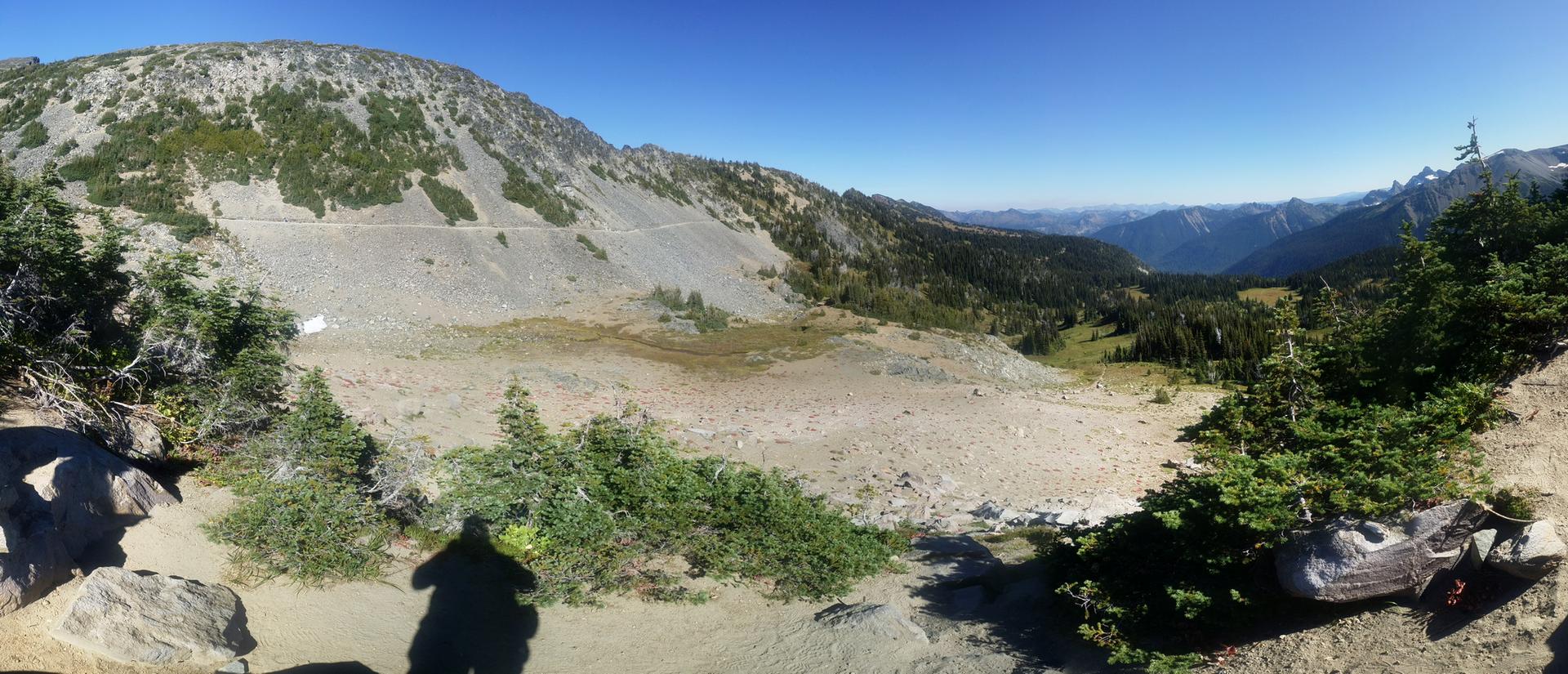Panoramic view of a rocky valley, distant mountains, with a person's shadow.