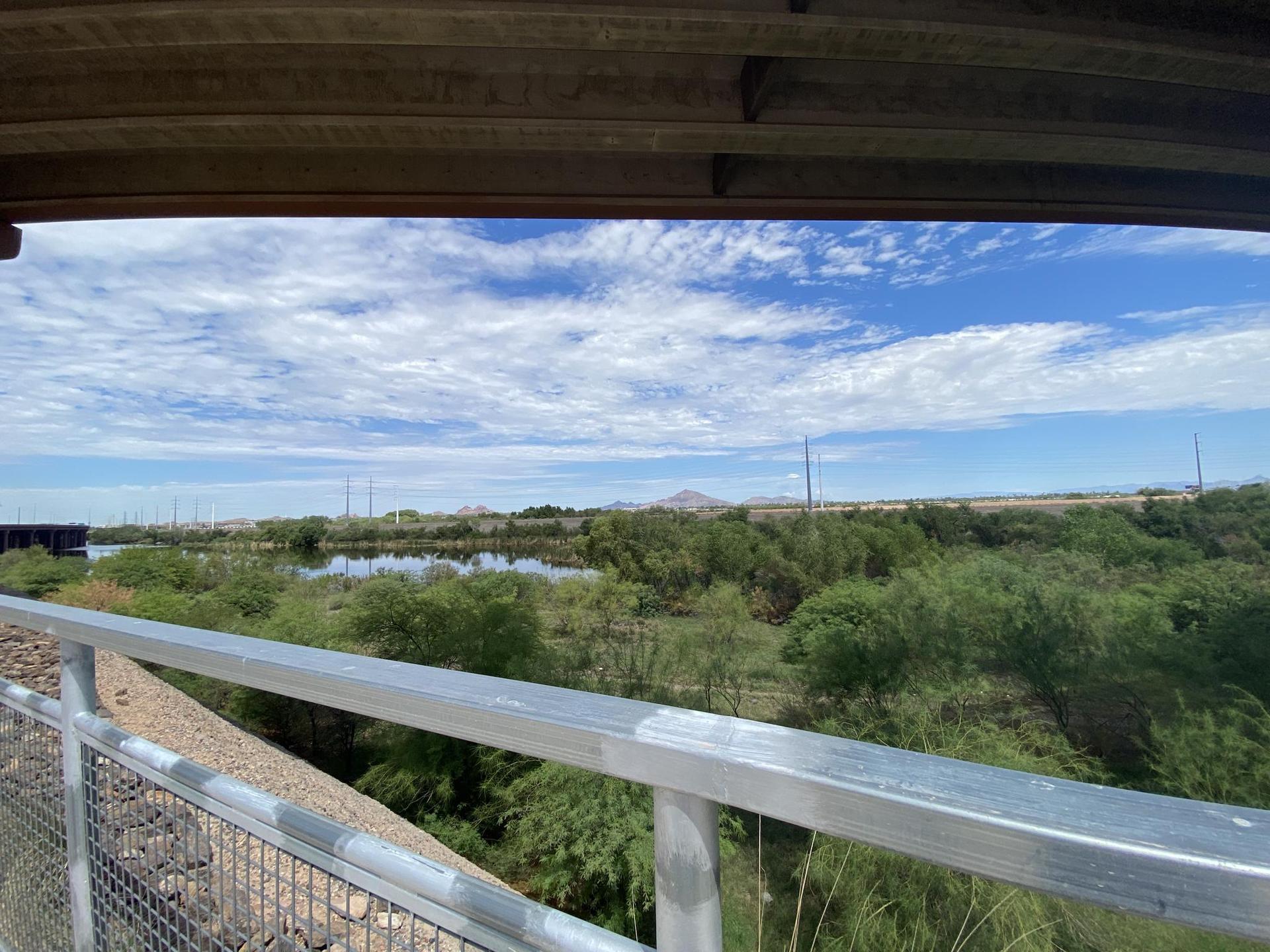 Overlook of a lush wetland with a lake under a bright, cloudy sky.