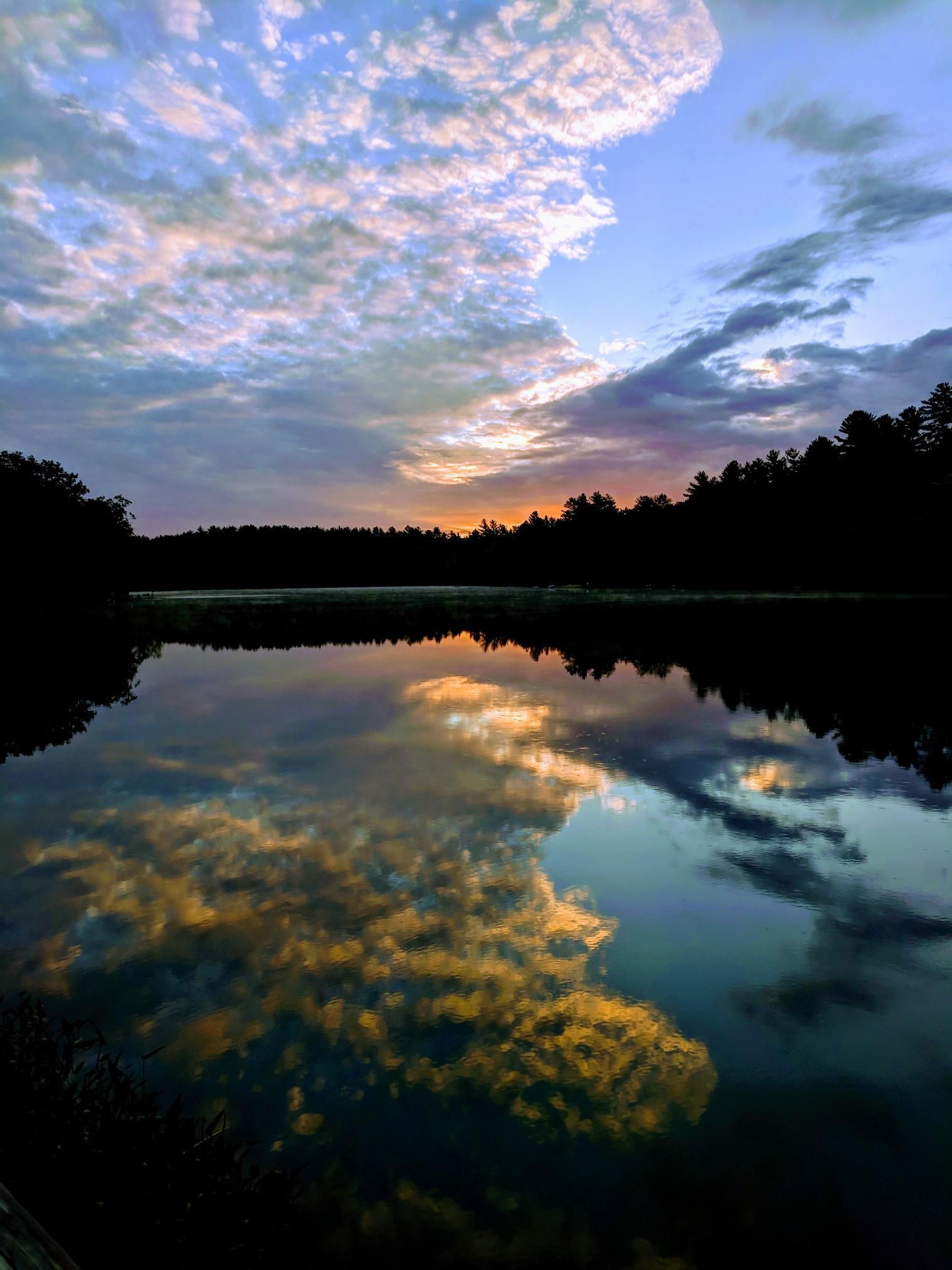 Serene lake reflecting a vibrant sunset sky with dark tree silhouettes.