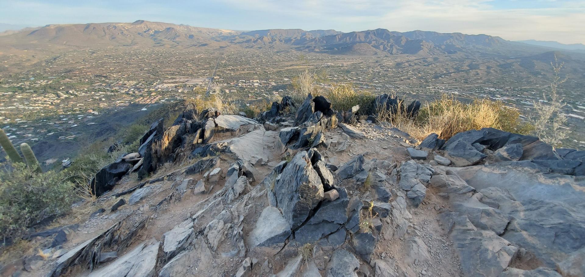Rocky mountain summit at golden hour, overlooking a sprawling valley.