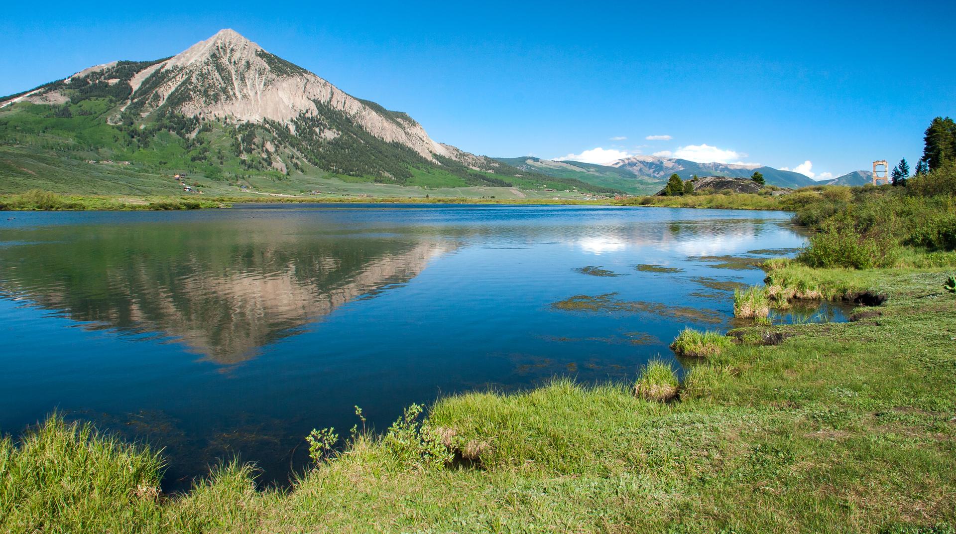 A majestic mountain reflects in a calm lake under a clear blue sky.