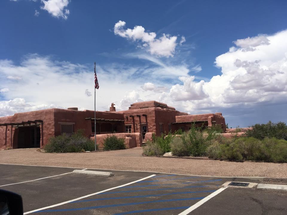 Red adobe building with an American flag, seen from a parking lot.
