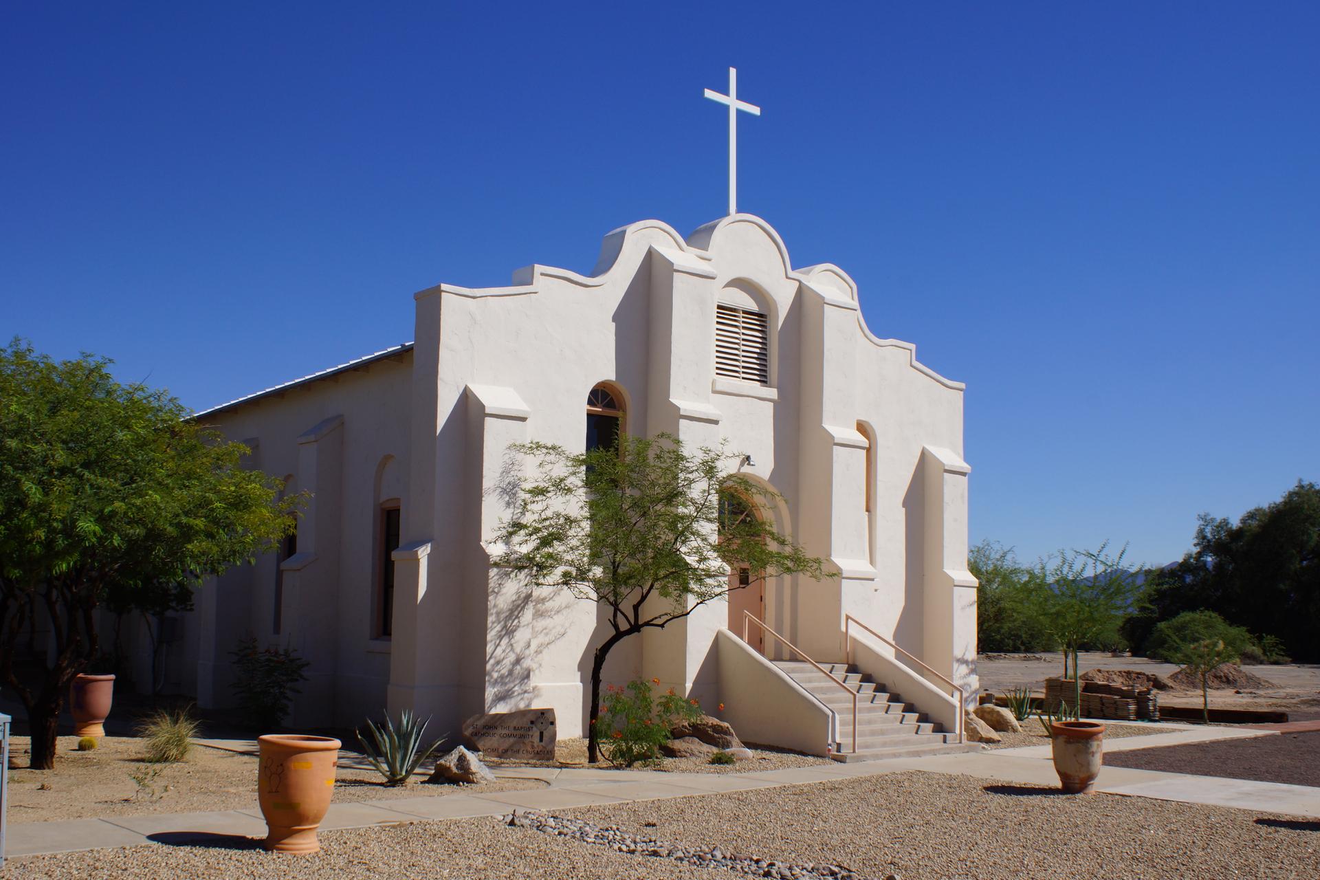 A white stucco church with a cross under a clear blue sky.