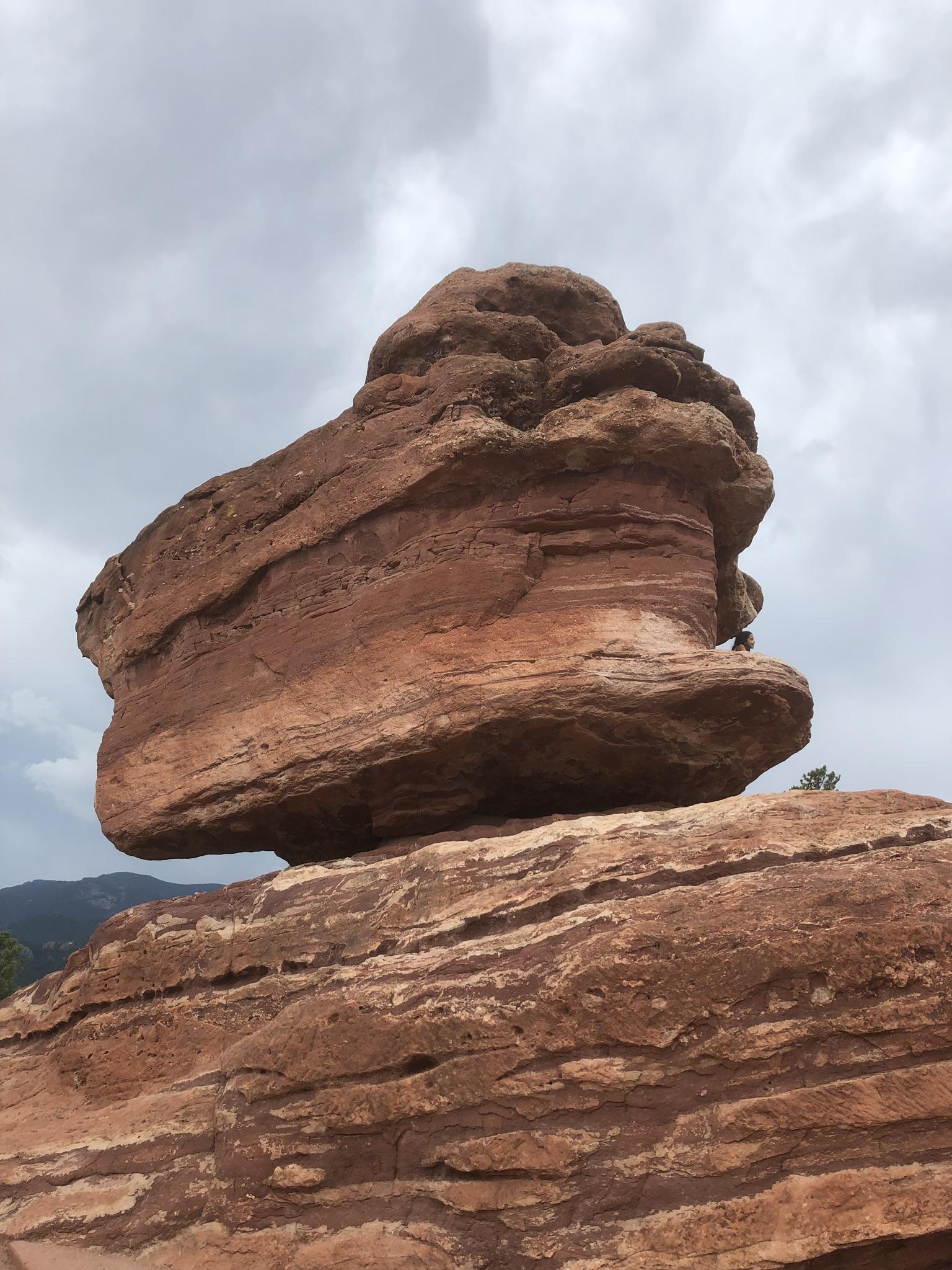 Unique balanced red rock formation against a cloudy sky.
