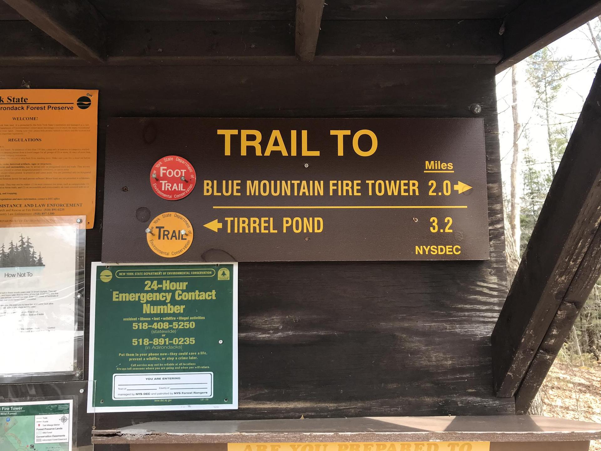 Brown wooden trail sign with white and yellow text, bright day.