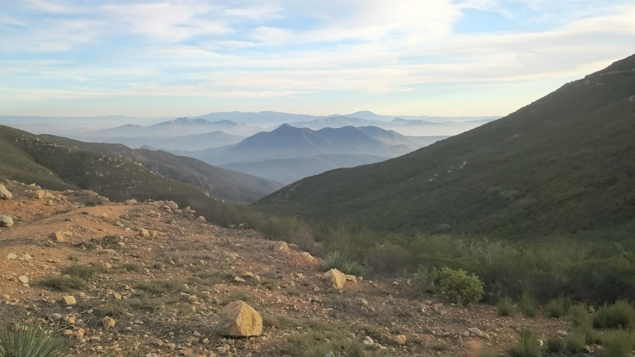 Hazy mountain valley with arid foreground and distant peaks under soft light.
