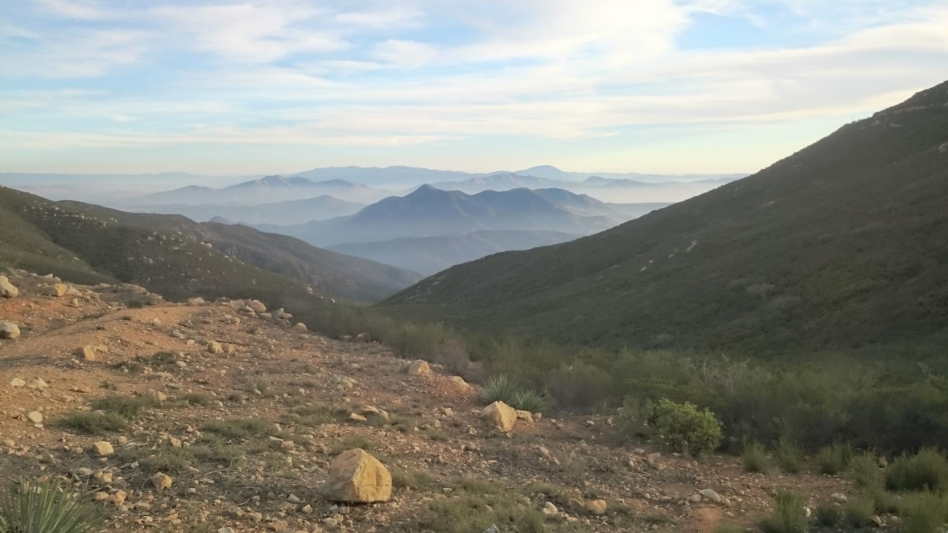 Hazy mountain valley with arid foreground and distant peaks under soft light.