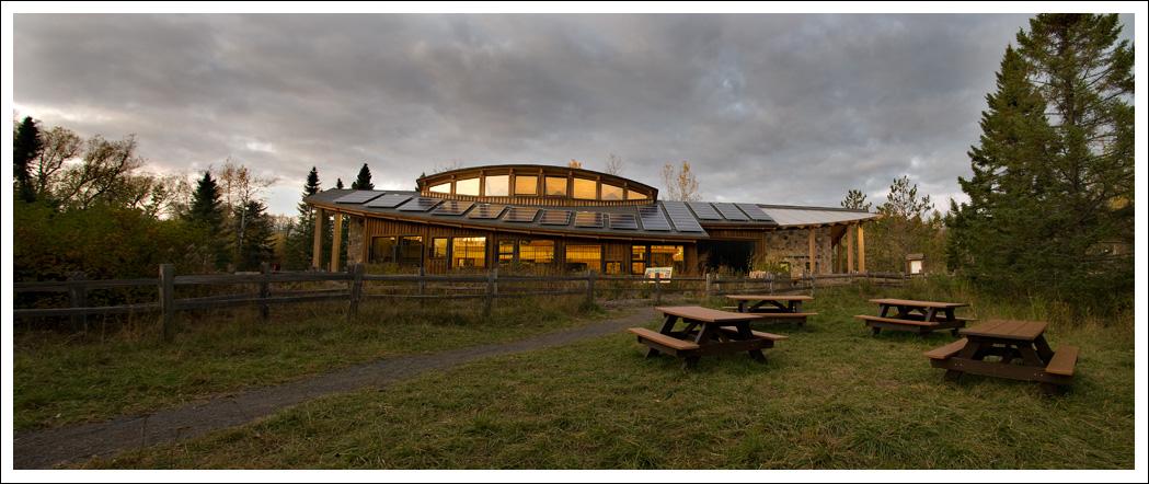 Modern building with picnic tables in a field under cloudy evening light.