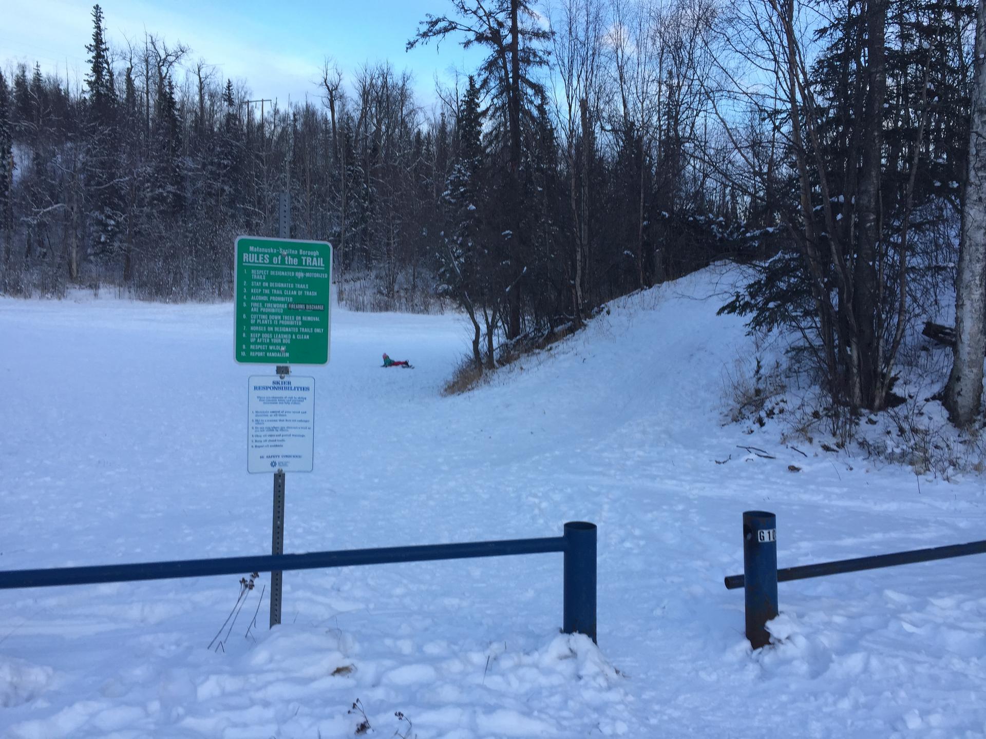 Snow-covered winter landscape with signs, a blue barrier, and a dense forest.