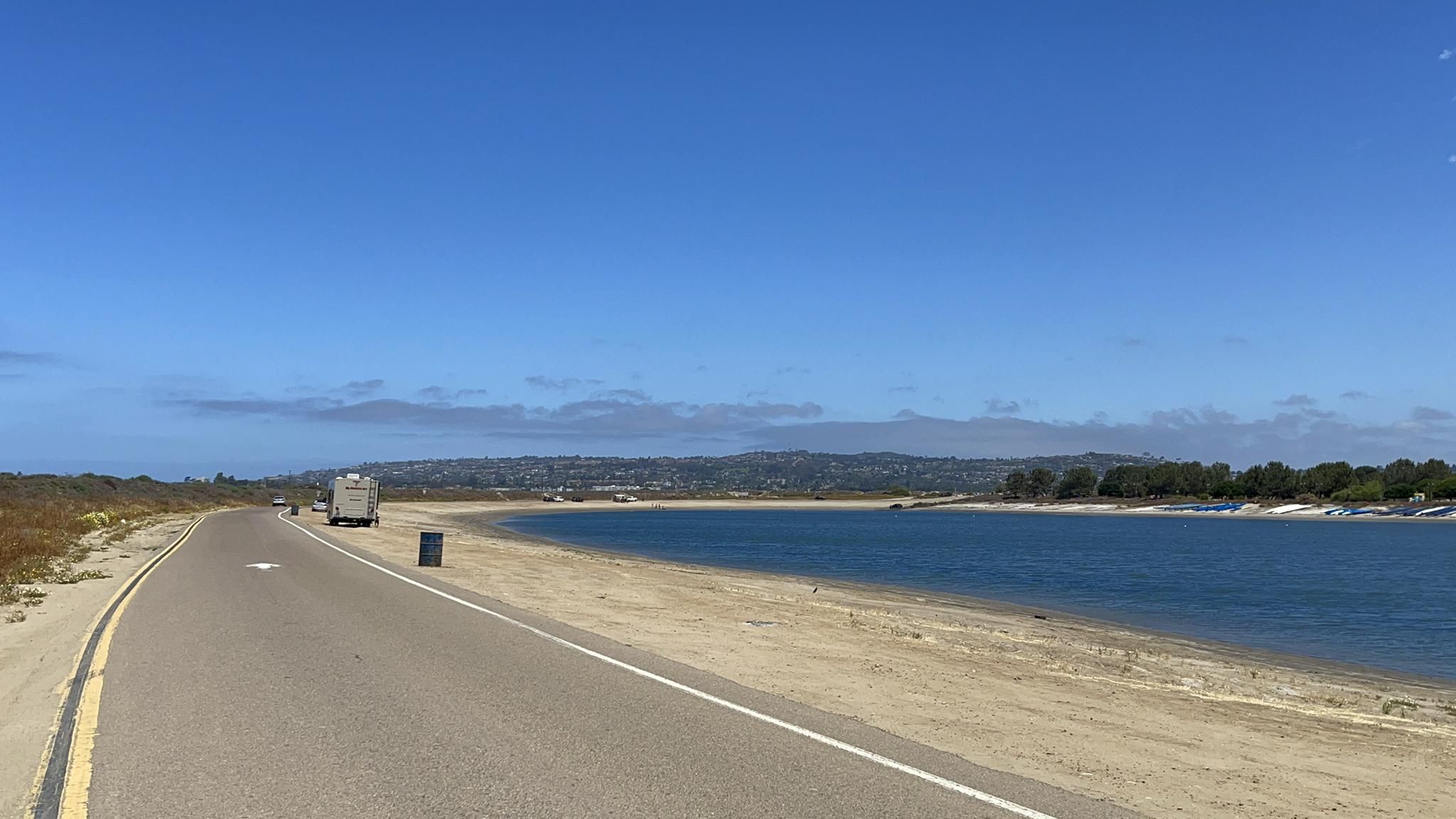 Paved road curves beside a blue bay, an RV parked nearby on a bright day. - Fiesta Island run loop