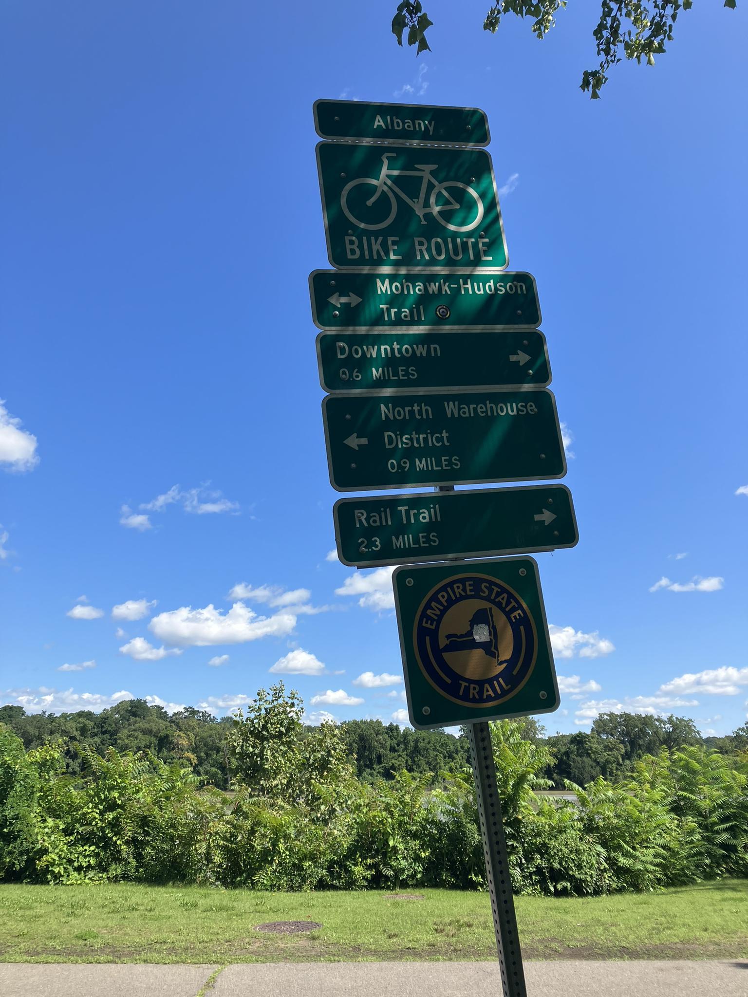 Green directional signs for a bike route against a blue sky.