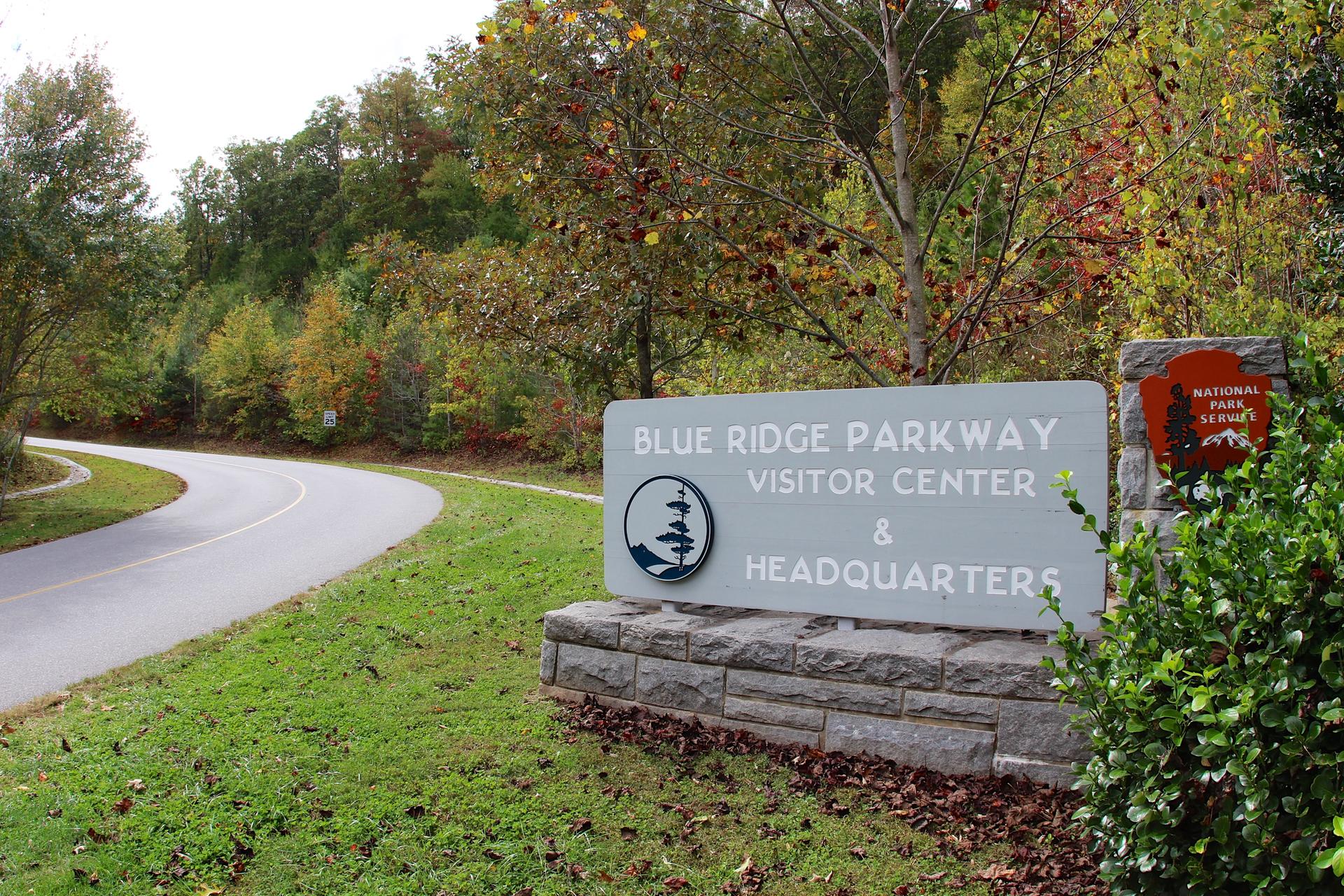 A large stone sign next to a curved road with autumn trees.