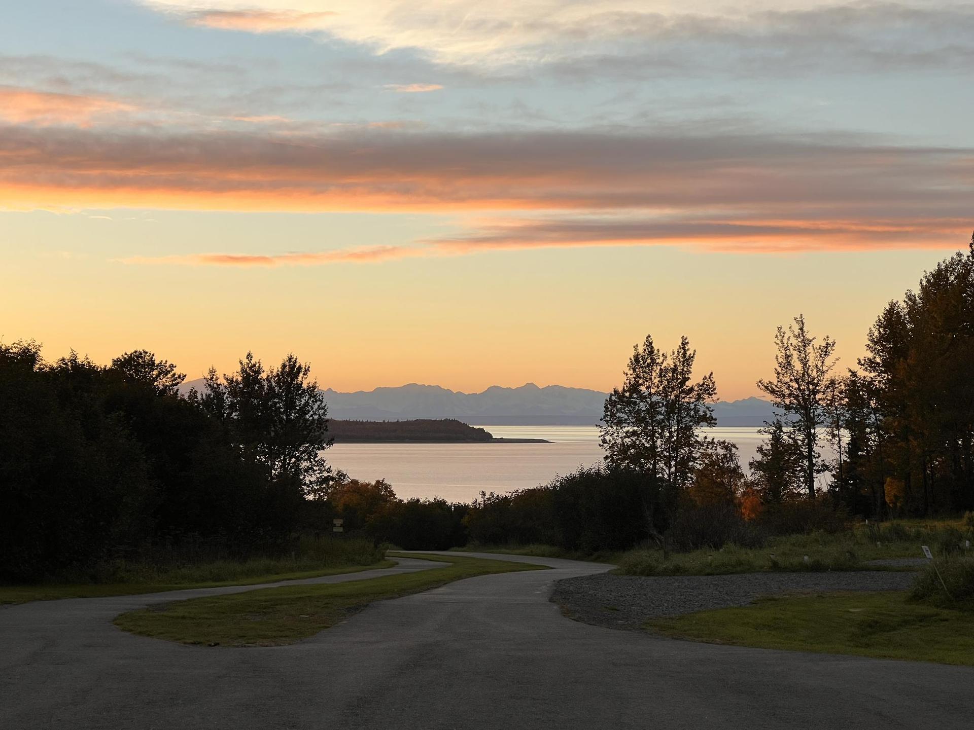 Dirt road leading to a calm body of water under a colorful sunset sky.