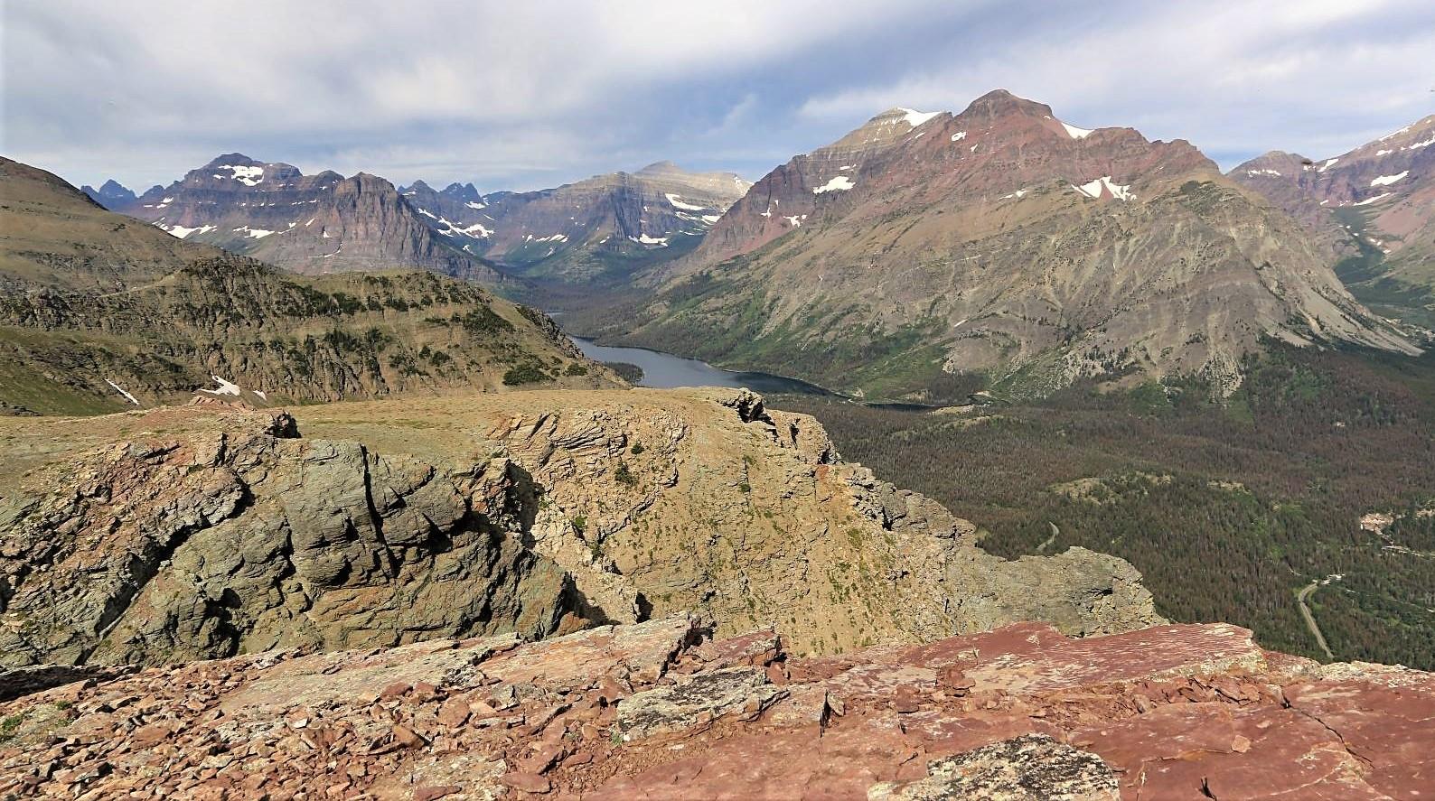 Expansive mountain vista with rocky foreground, distant peaks, and cloudy sky.