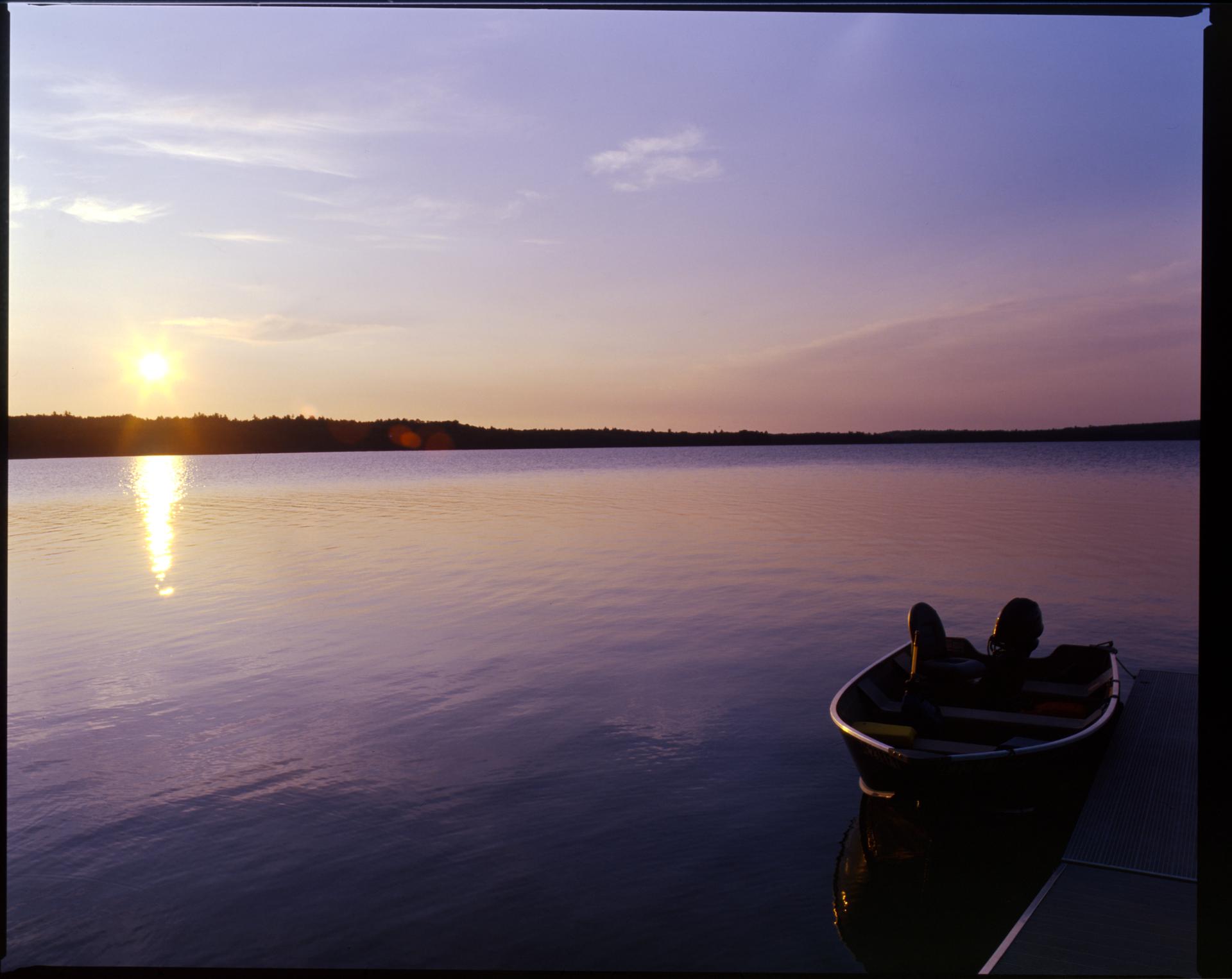 Sunset over a tranquil lake with a small boat docked nearby.