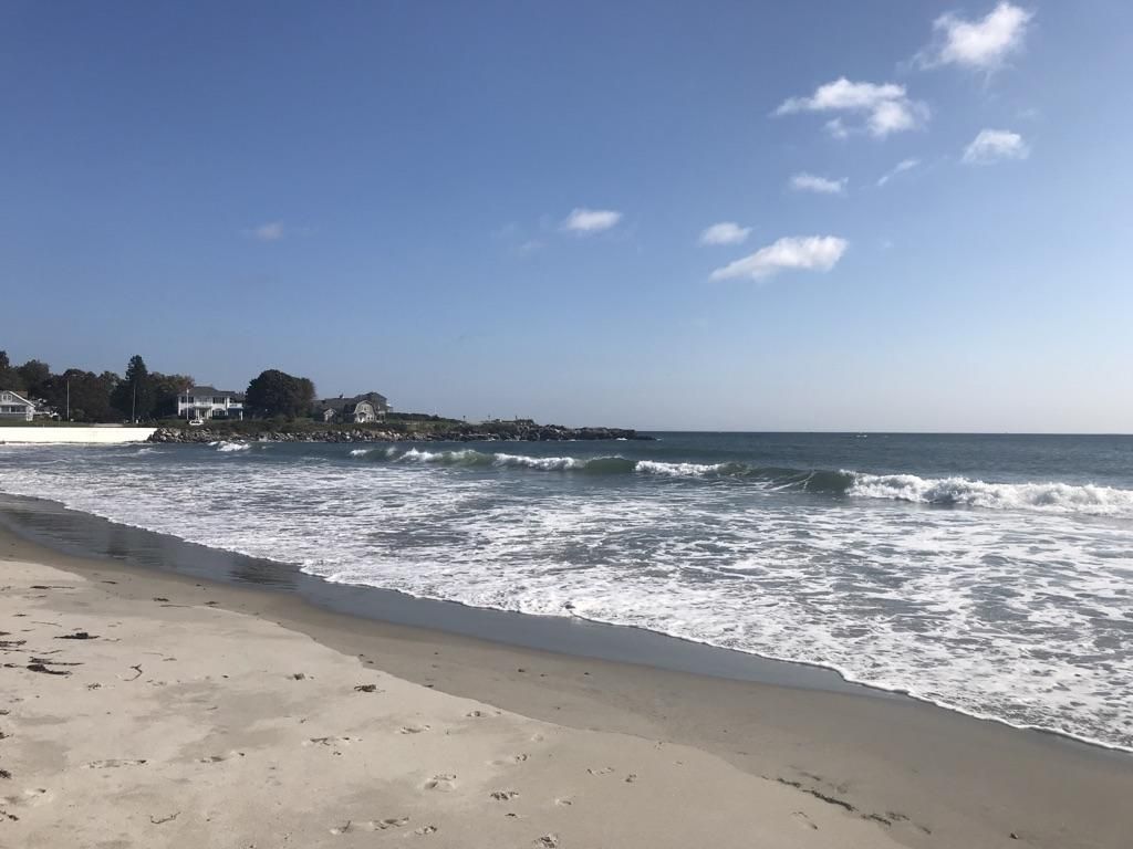 Sunny beach with white waves crashing on the sand, distant houses. - Hampton Beach to Ocean Boulevard and Wallis Sands Beach loop
