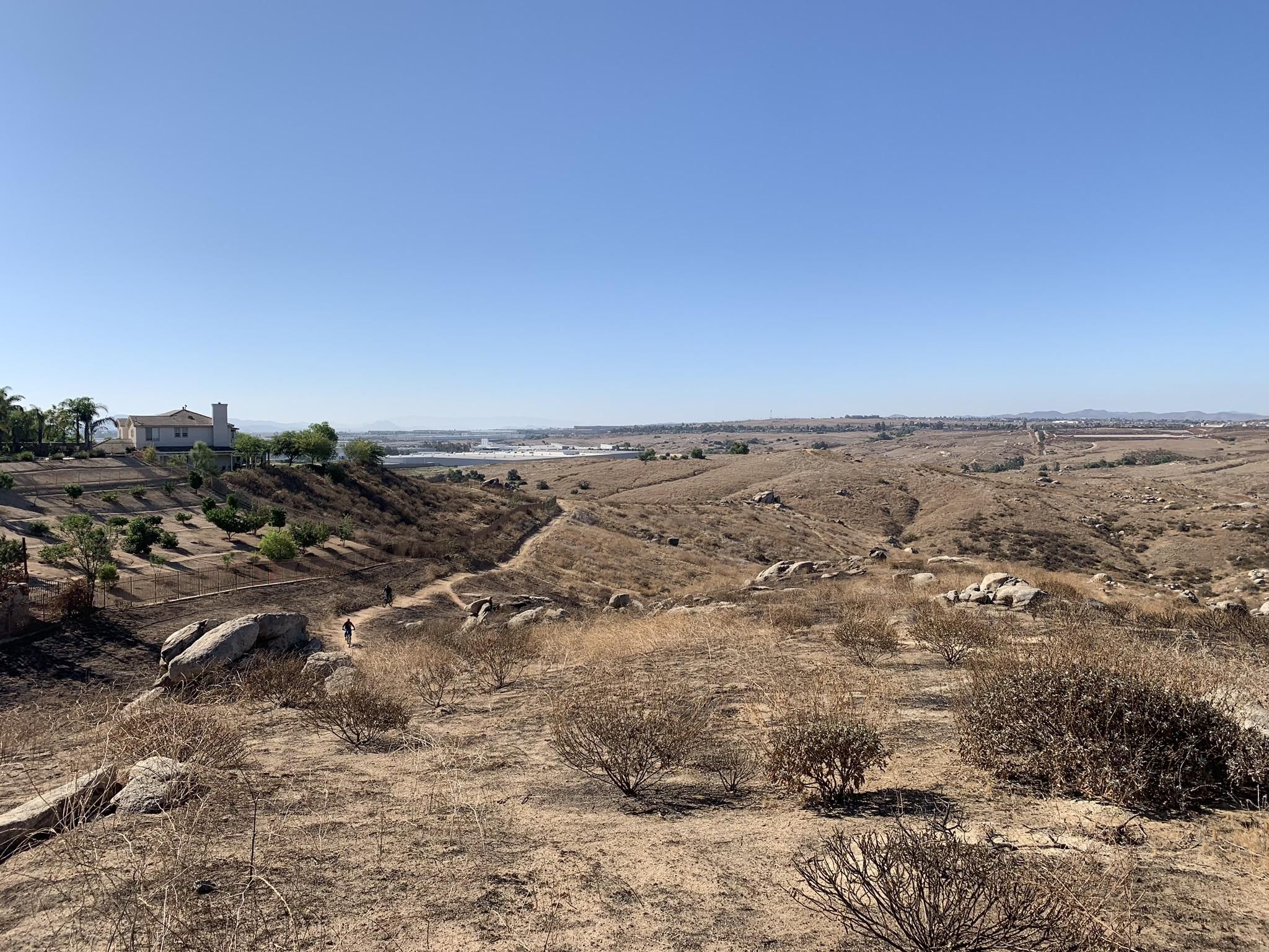 Expansive dry hills under a clear sky with distant buildings and hikers. - Sycamore Canyon Trail loop