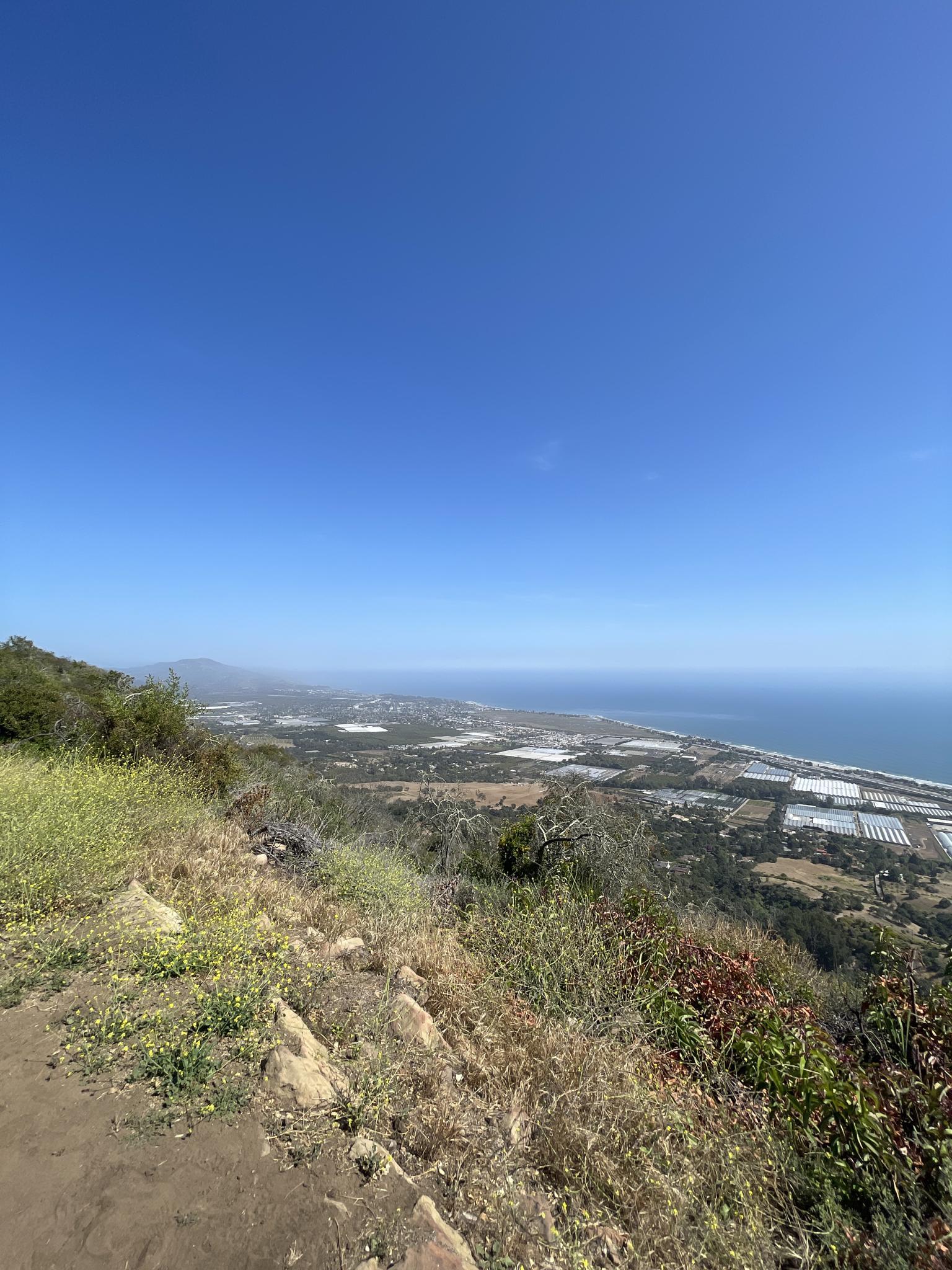 Bright, clear day over a coastal valley with fields and the ocean.