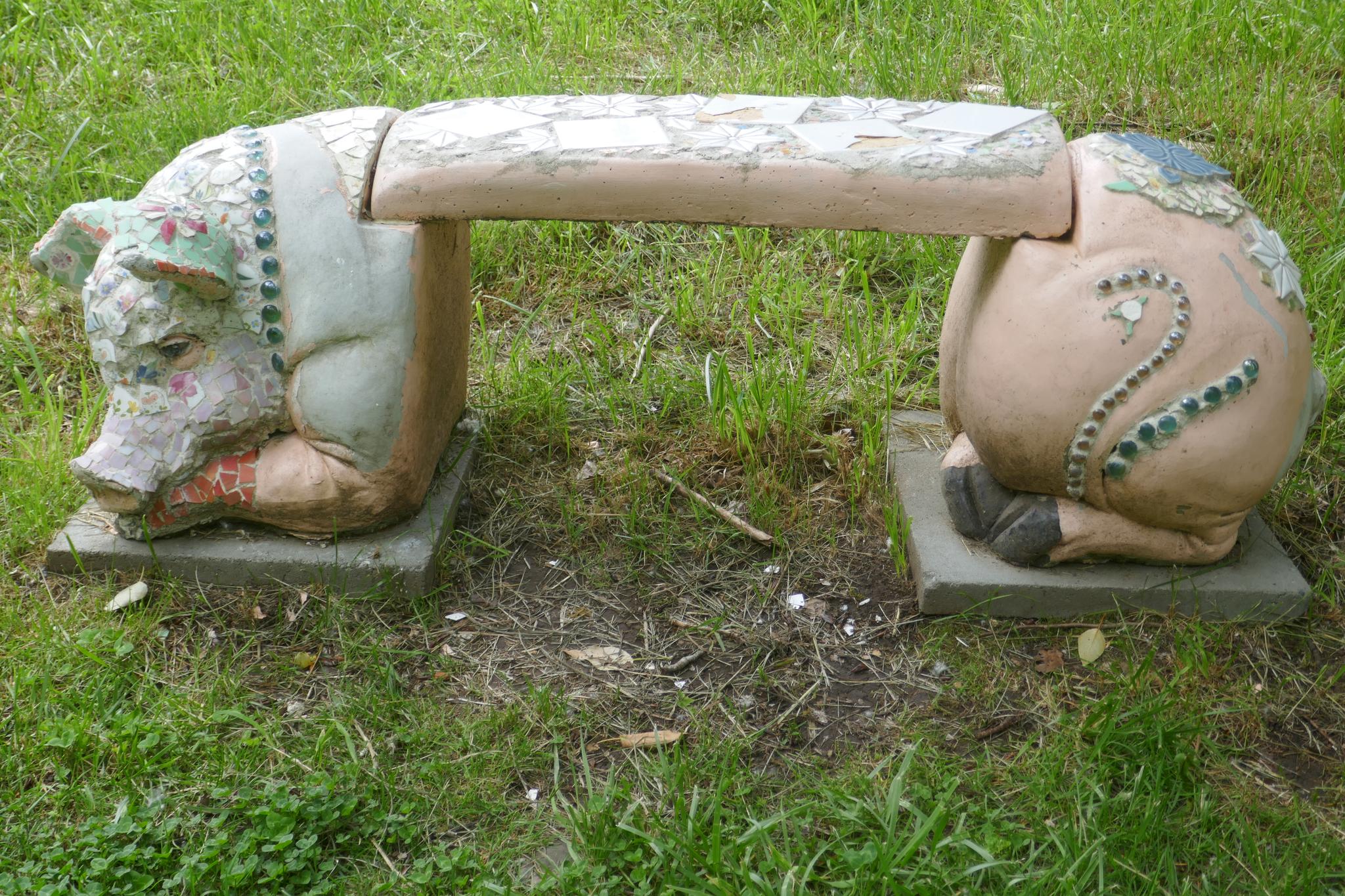 A whimsical pig-shaped concrete bench sits on green grass in bright light.
