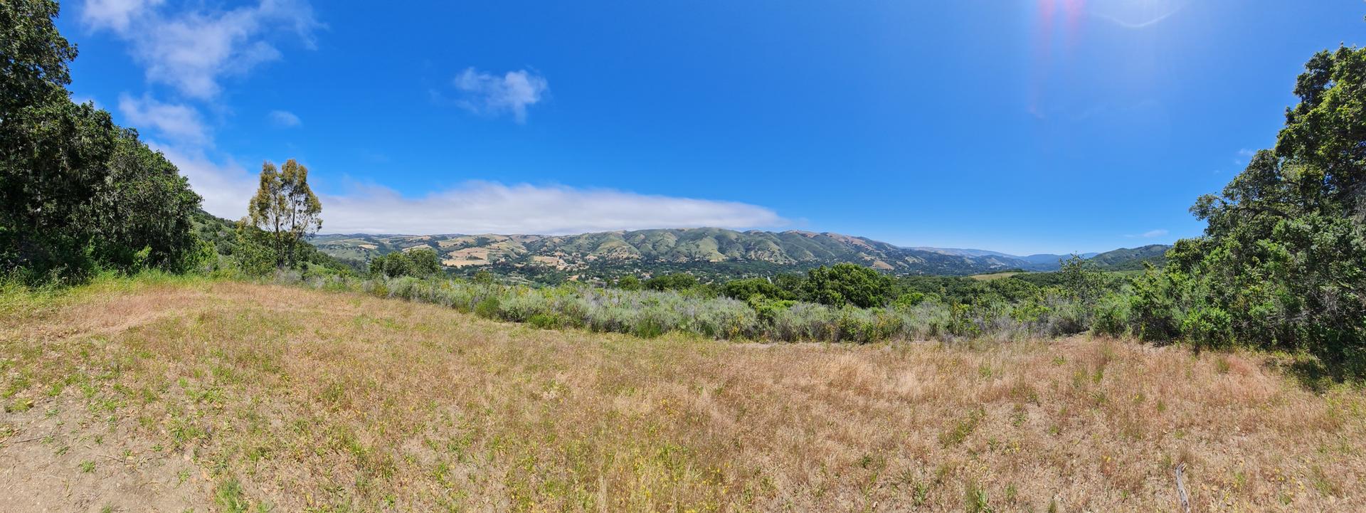Panoramic view of a vast valley with dry grass and distant green hills.