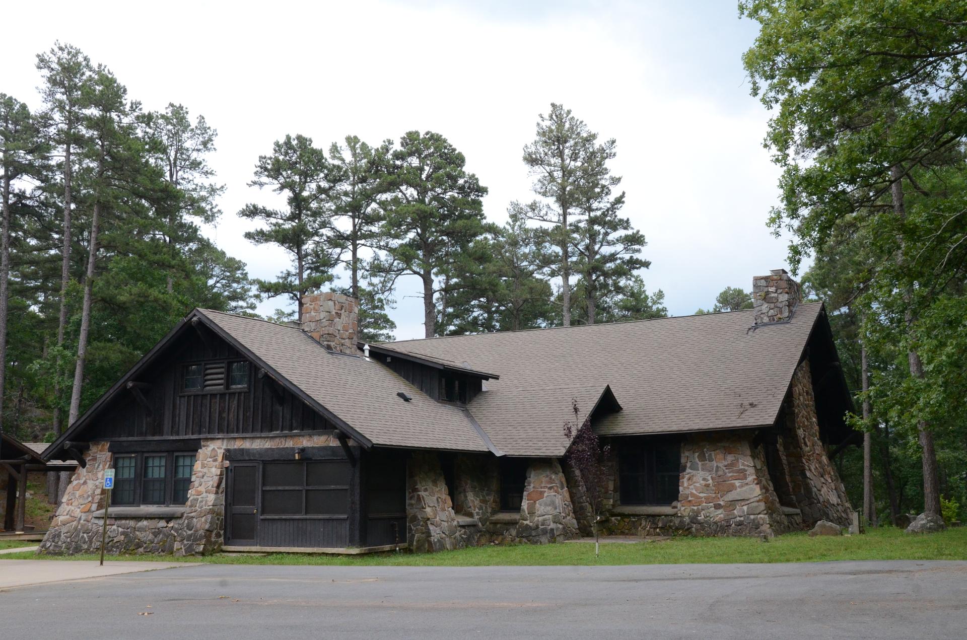Rustic stone and wood building with a complex roof, surrounded by tall trees.