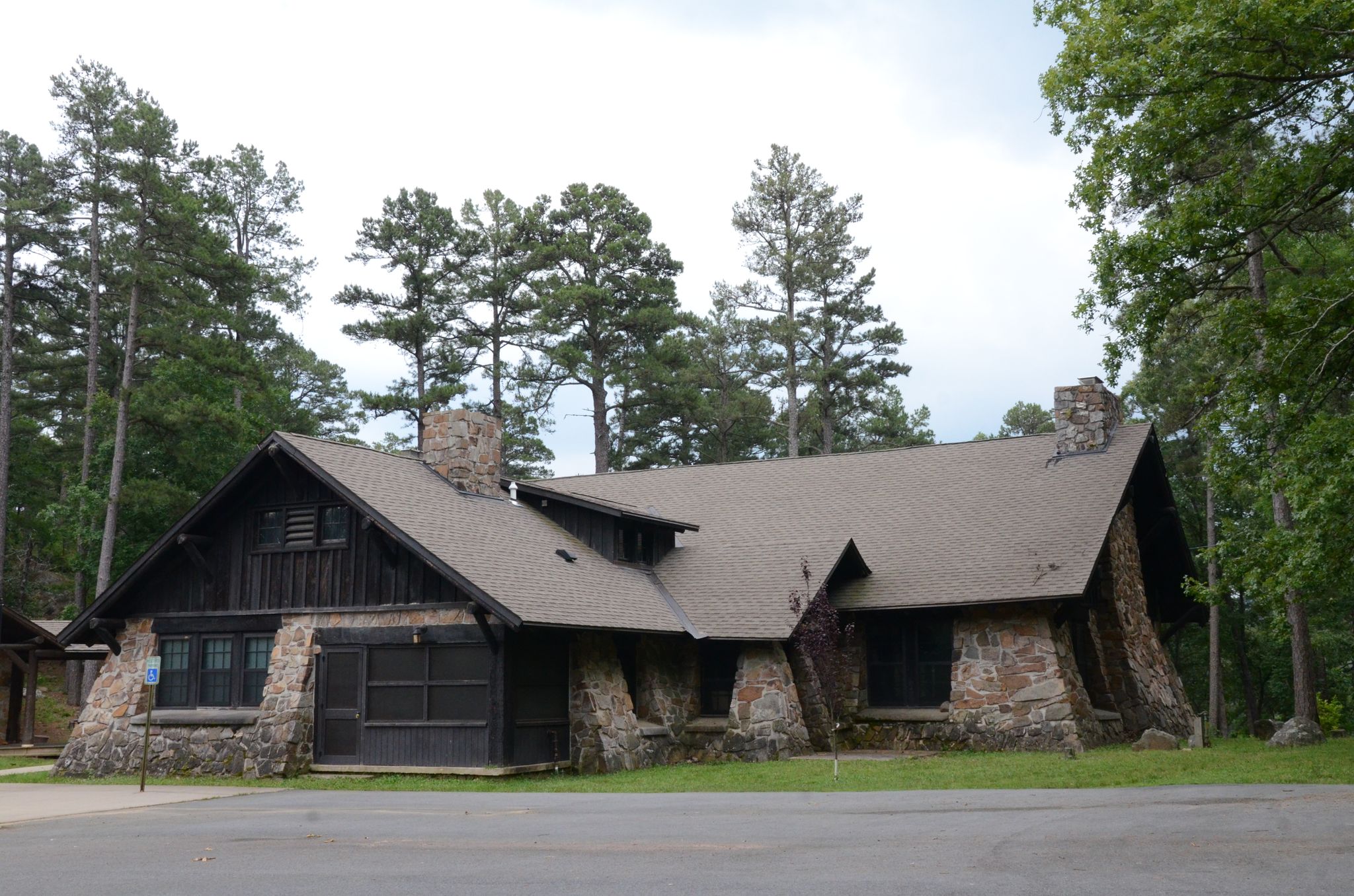 Rustic stone and wood building with a complex roof, surrounded by tall trees. - Ouachita and Lake Sylvia Trail