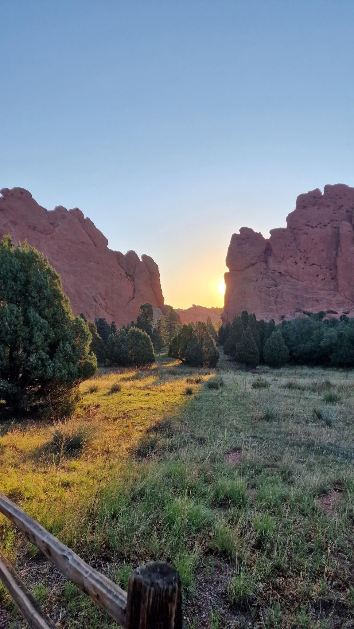 Golden sunrise illuminates a narrow gap between towering red rock formations.