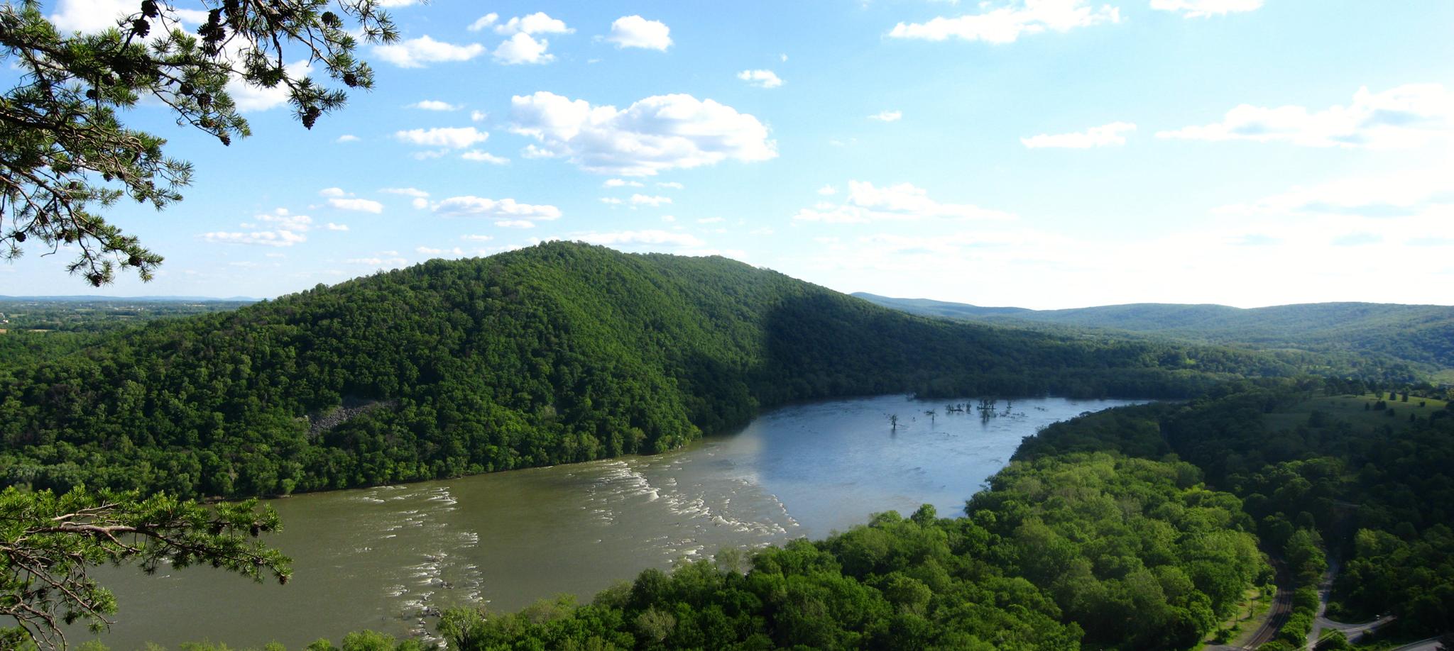 Panoramic view of a wide river winding through lush green, forested mountains.