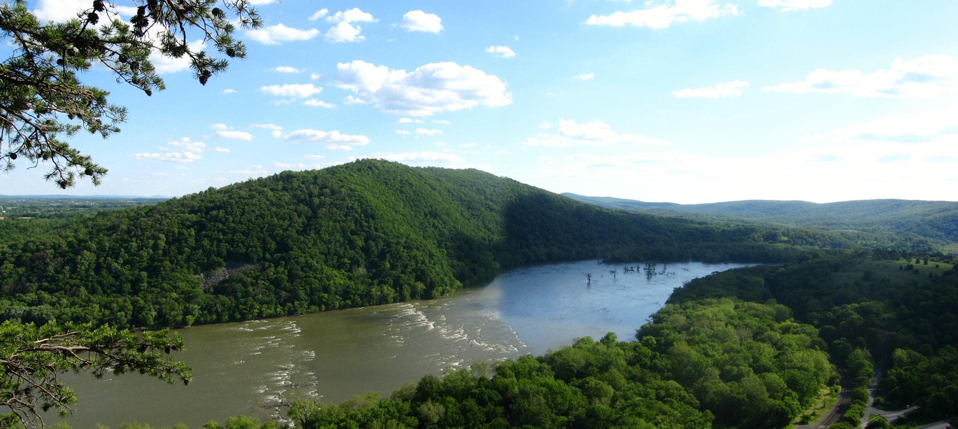 Panoramic view of a wide river winding through lush green, forested mountains.