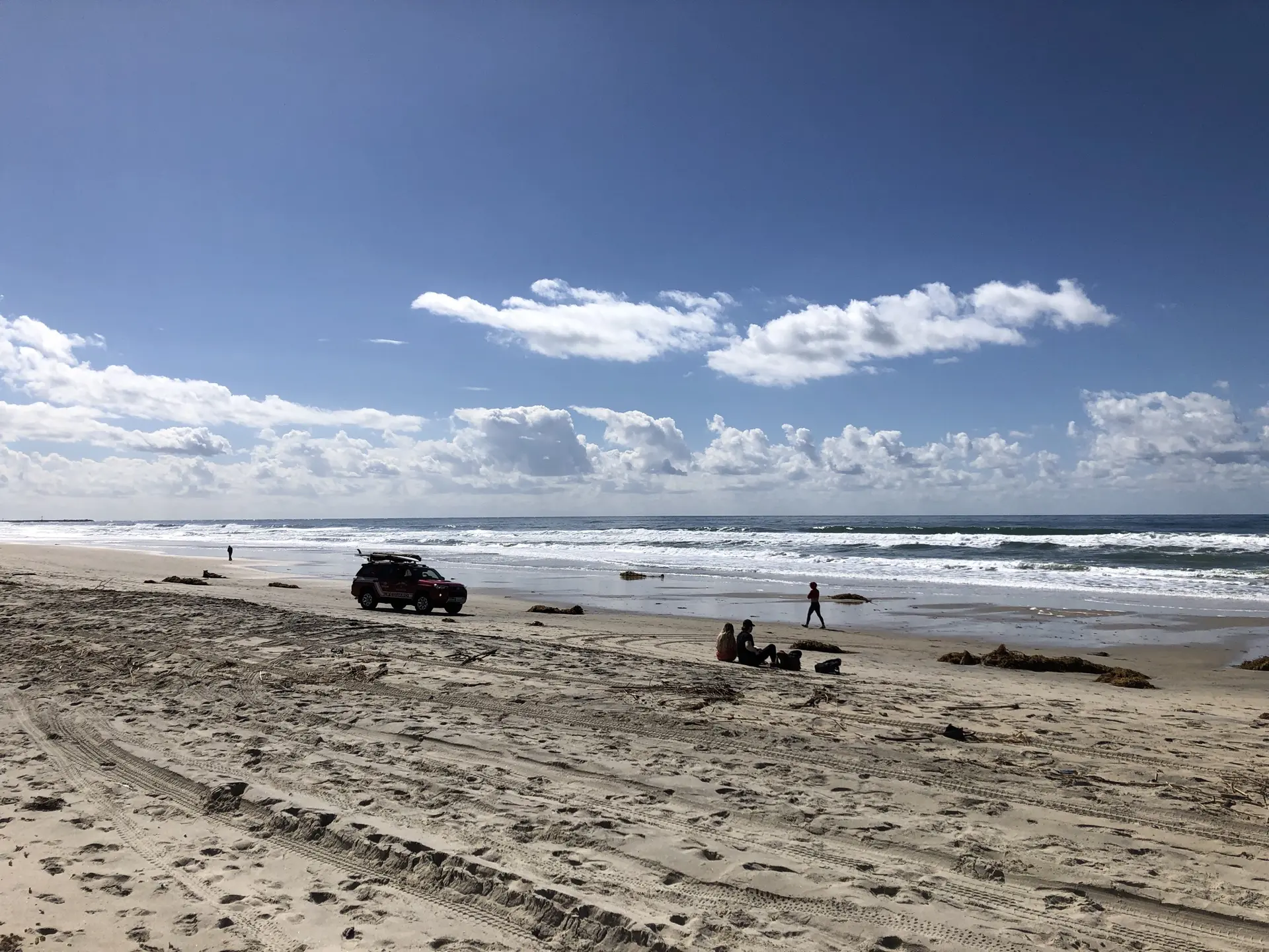 Bright day on a wide sandy beach with ocean waves and people.