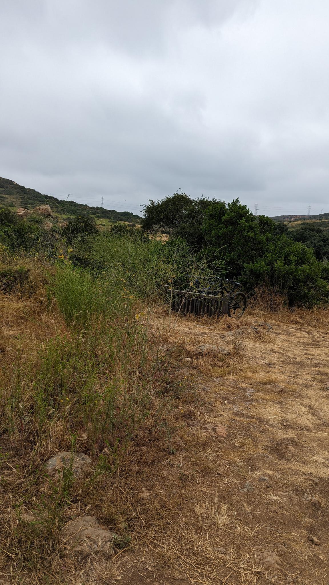 Overcast sky above dry, grassy hills with green bushes and a bike rack.